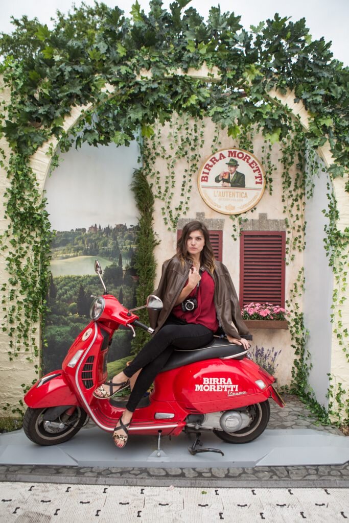  woman in leather jacket sat on red moped under archway 