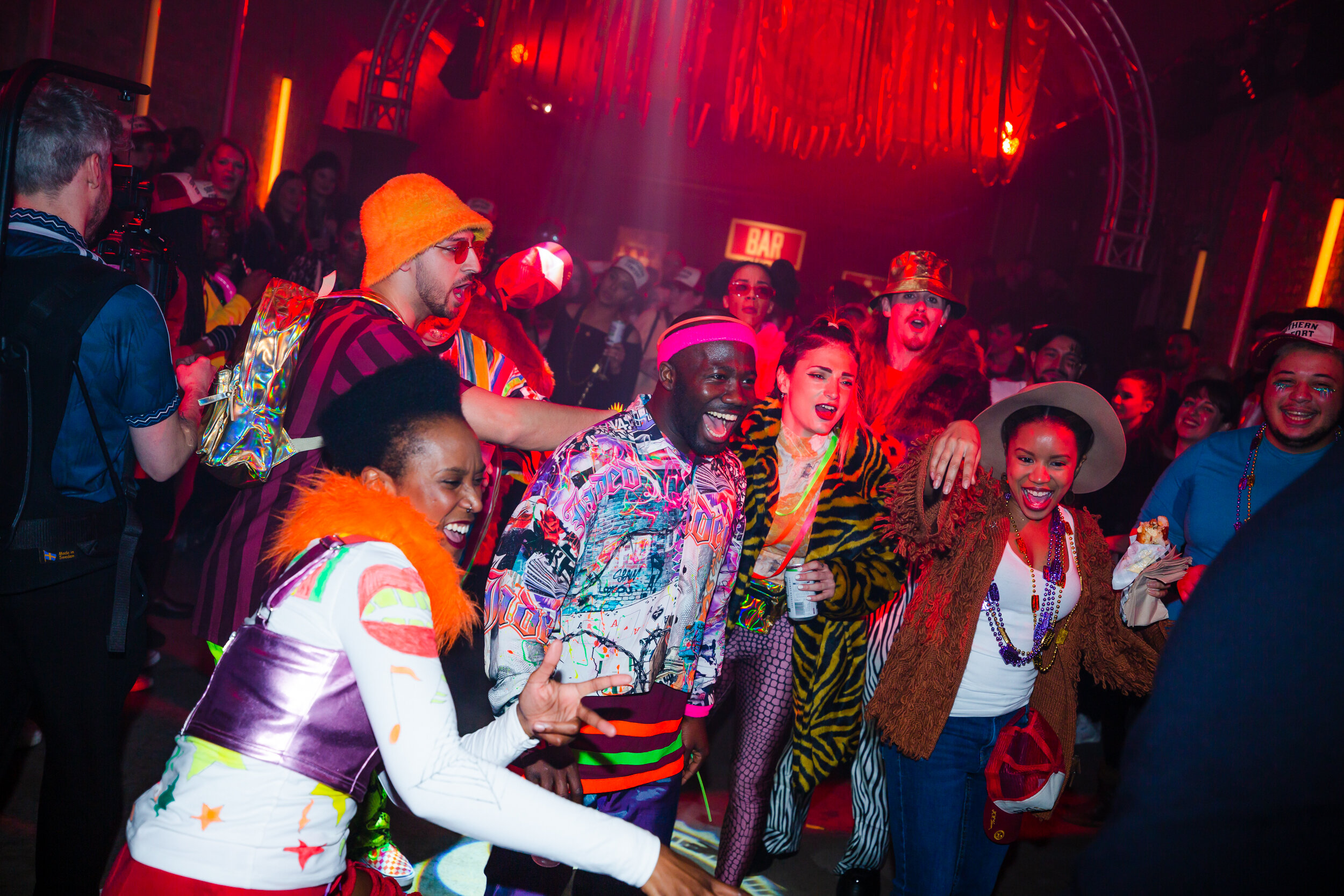  Friends raving together all dressed in a sea of fluro dancing and encourage others to get on the dance floor 