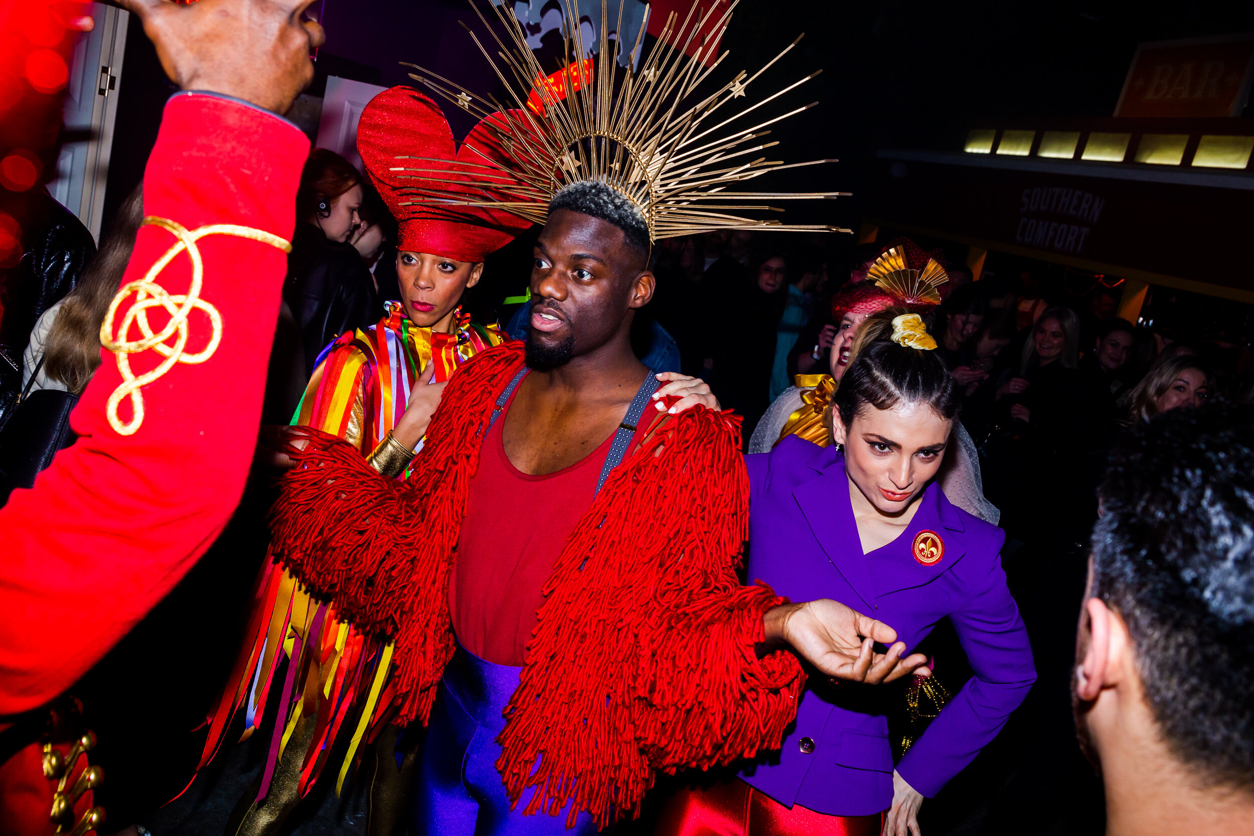  fabulous queen wearing a gold crown an purple fringe jacket stands with his entourage and faces off with his fremeny 