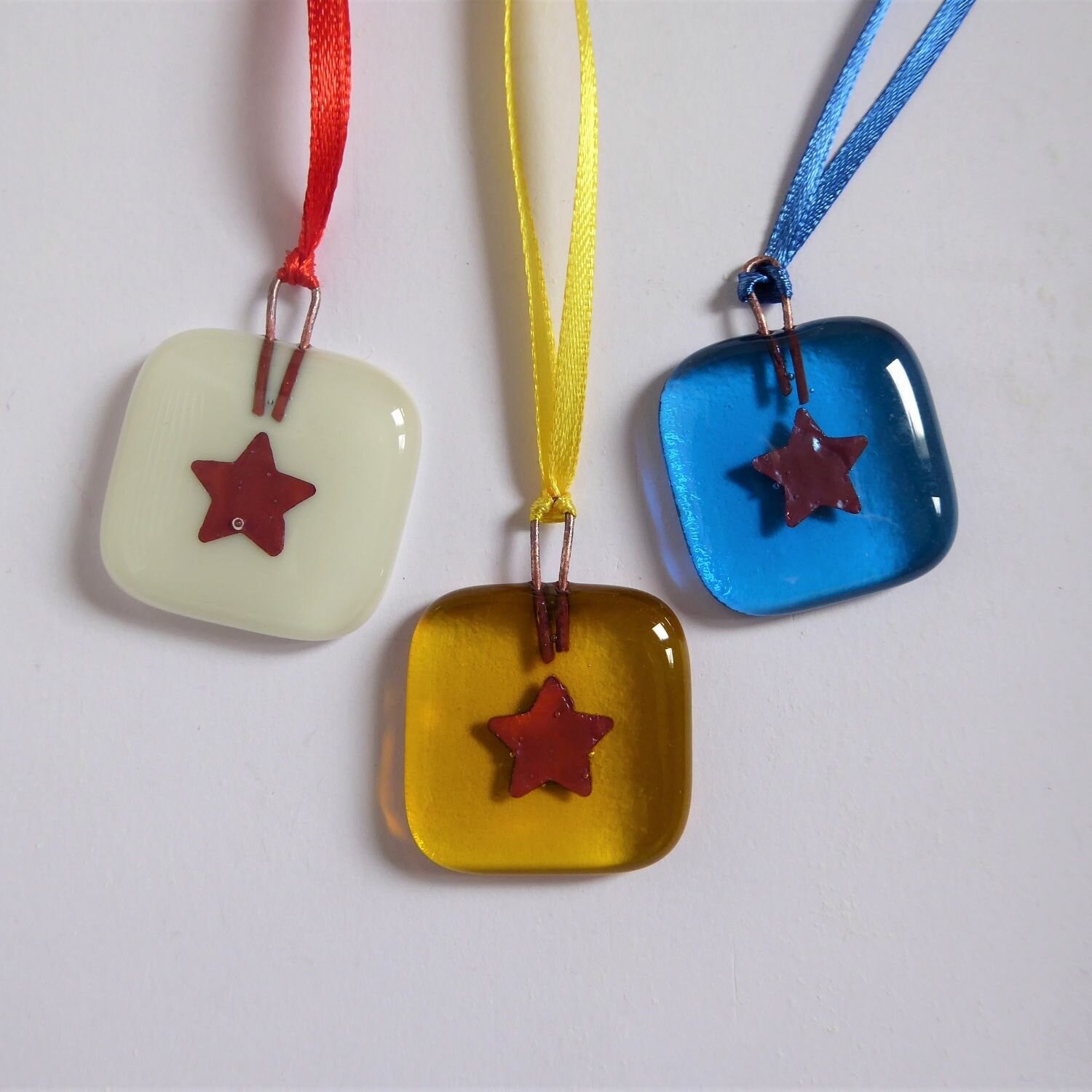  A set of three small square Christmas tree decorations by Eva Glass Design with a copper motifs on colourful backgrounds. 