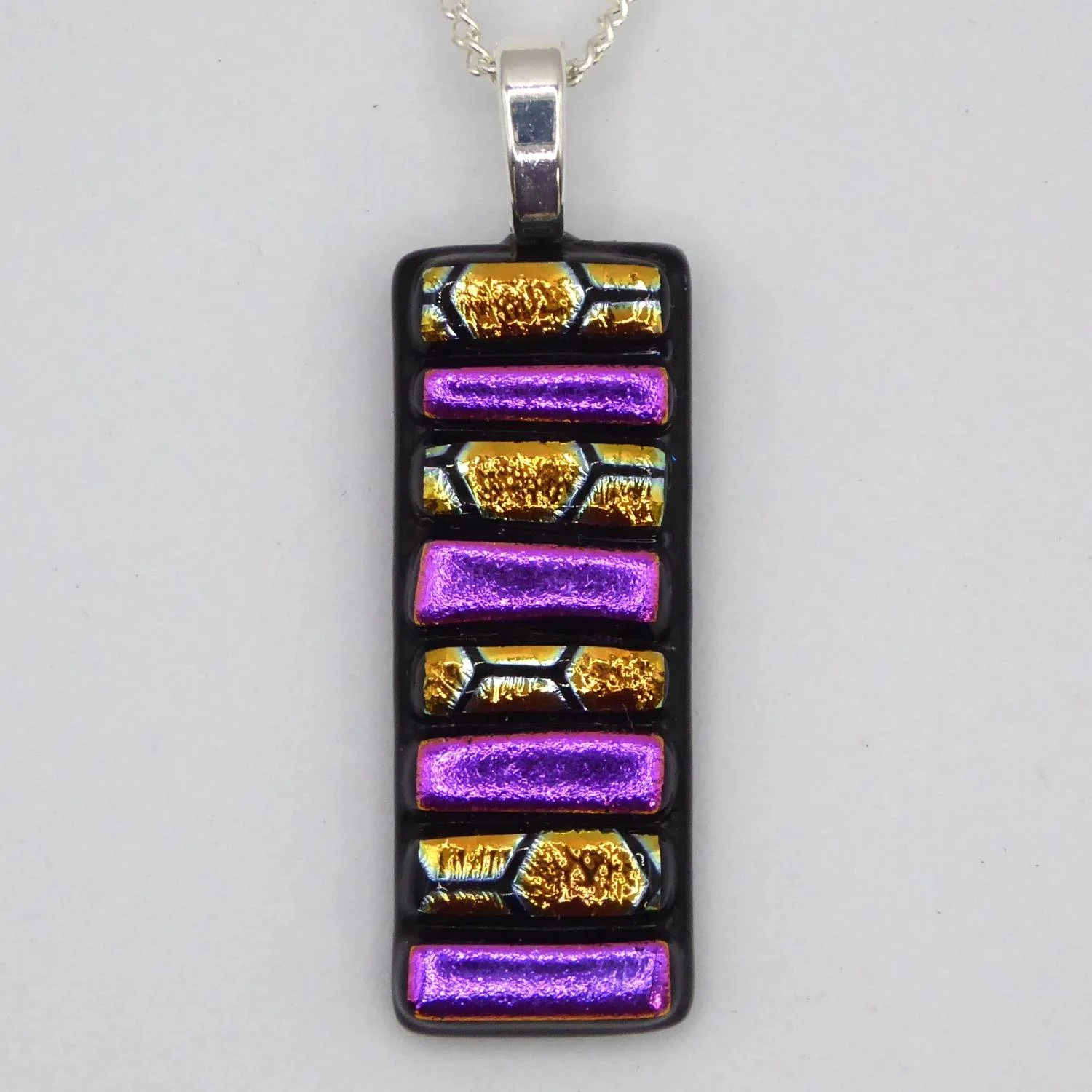  Fused glass pendant with strips of pink dichroic glass fired onto a black background. 