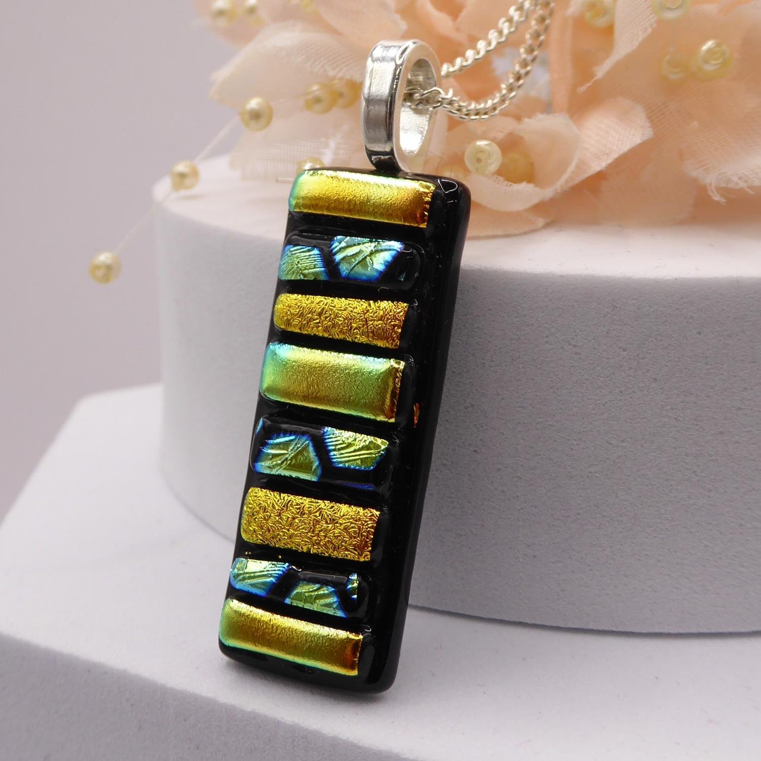  Gold fused glass pendant handmade using strips of dichroic glass with gold tones and patterns fired onto a black background. 