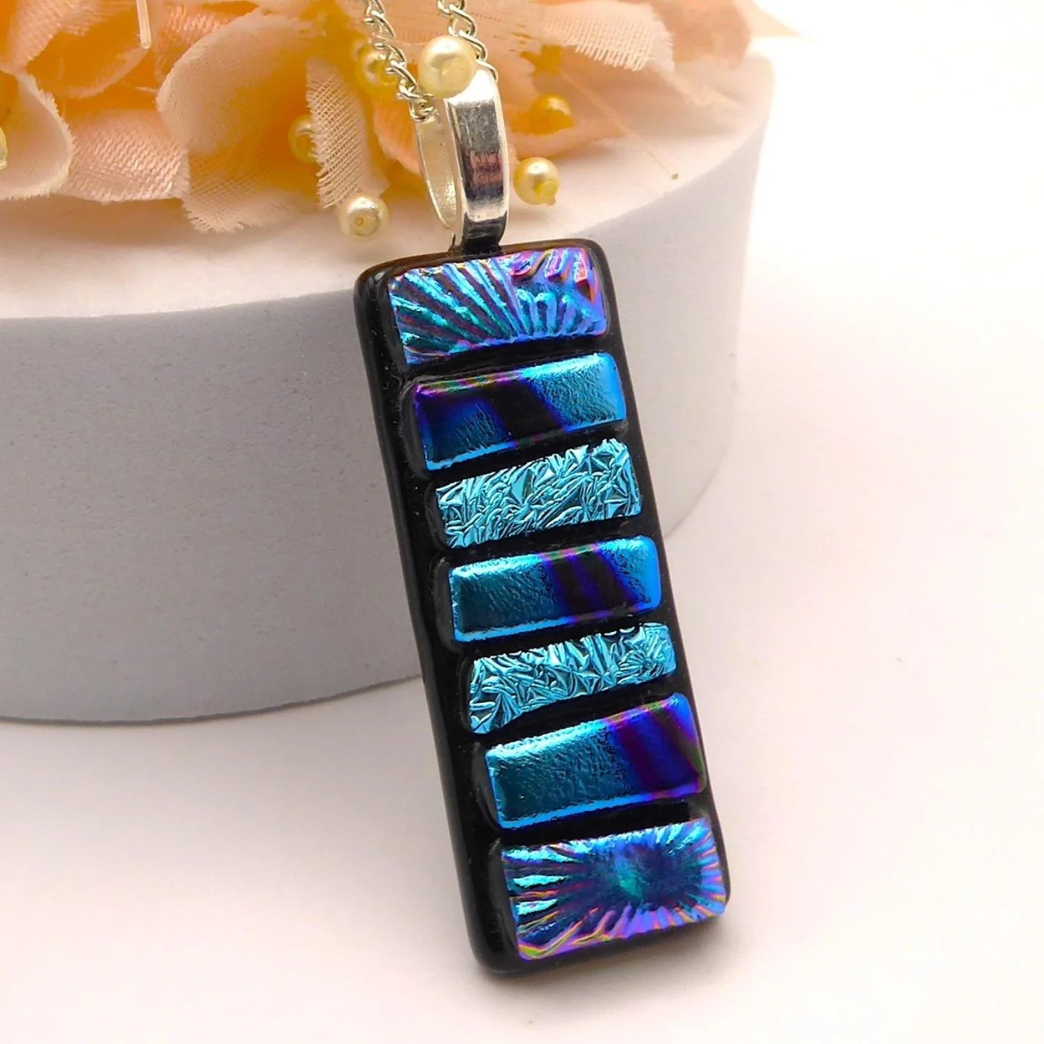  Fused glass pendant with strips of patterned and textured pale blue dichroic glass fired onto a black background 