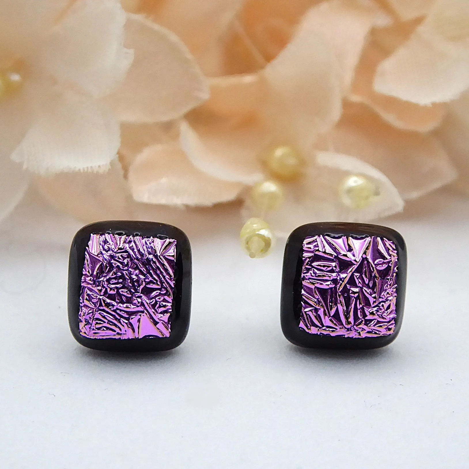  Square fused glass earrings in a stud style with shimmering pink dichroic glass on a black background 