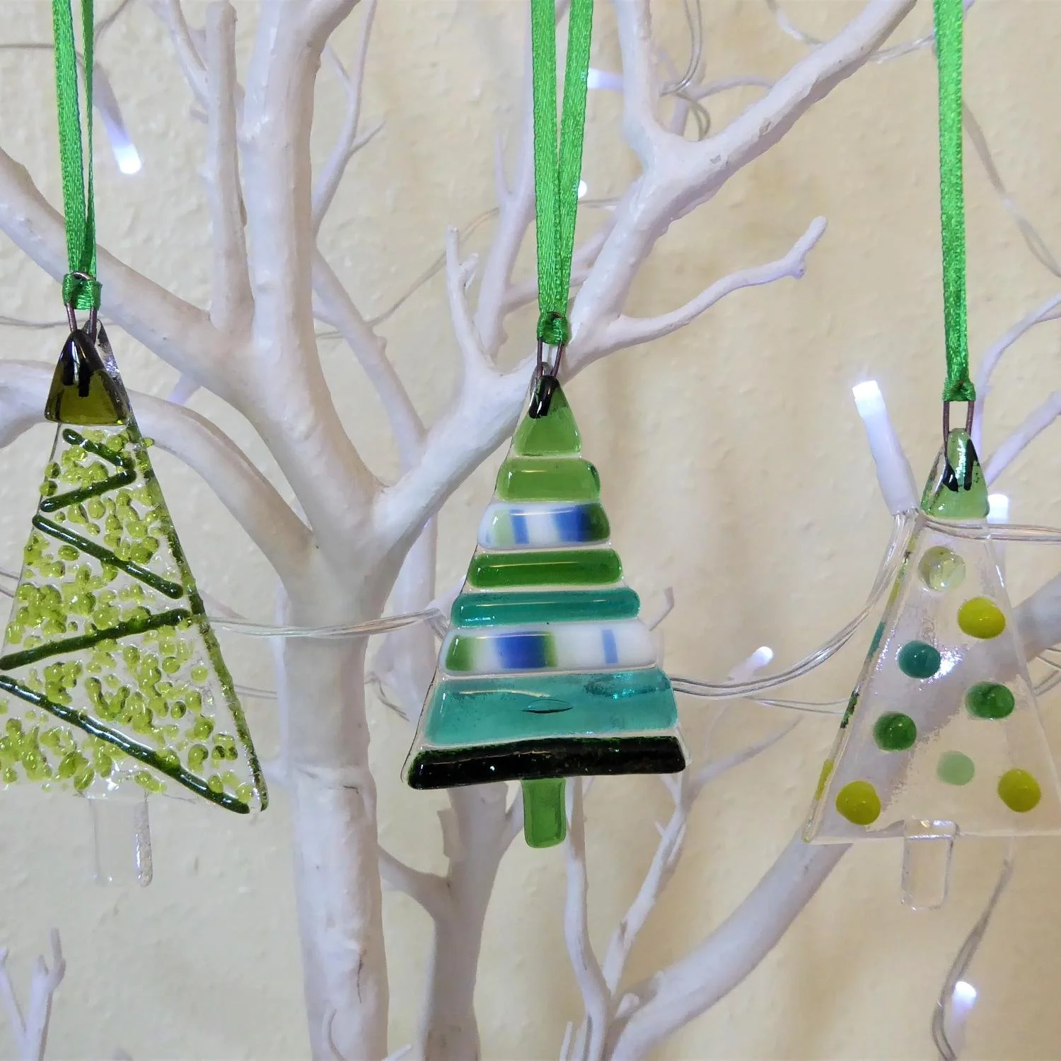  Three hanging tree-shaped Christmas ornaments with designs made from green glass fused onto clear glass 