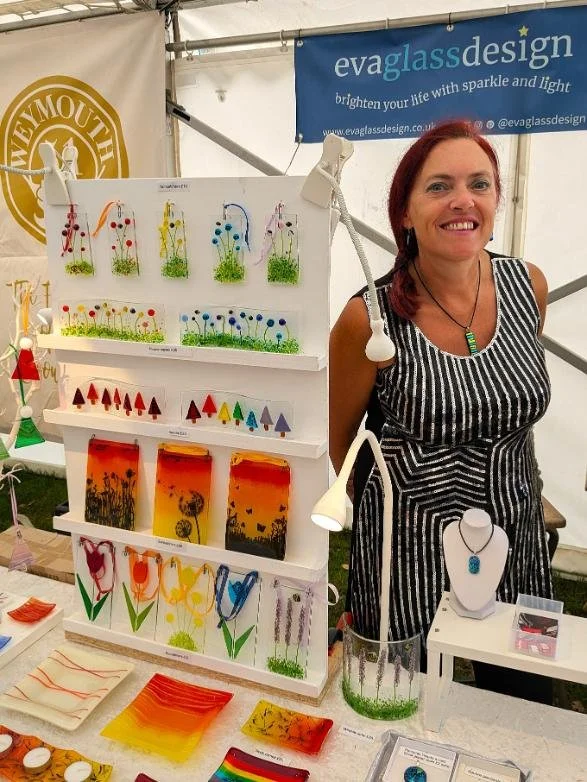 Artist Eva Pollard standing behind her stall at an event with colourful fused glass products