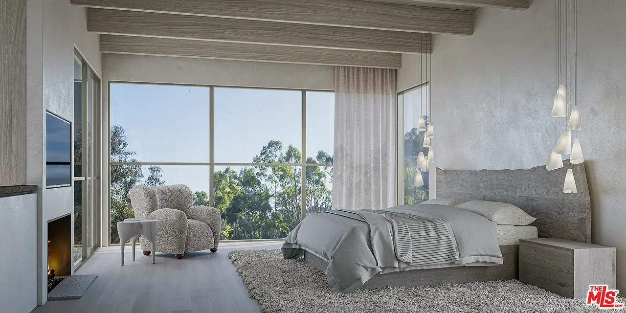 Modern bedroom with large window, view of trees, bed with gray bedding, white armchair, side table, hanging pendant lights, and a fireplace