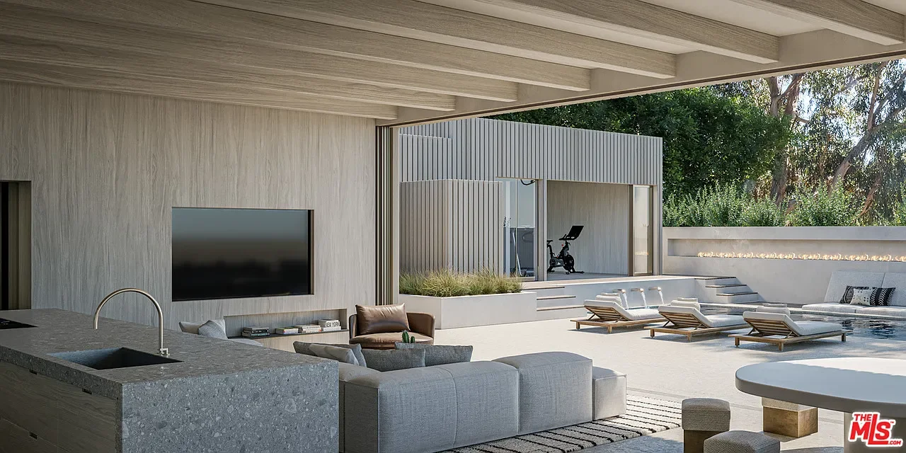 Modern outdoor living space with a covered lounge area, flat-screen TV, a sectional sofa, a small armchair, a large round dining table, wooden lounge chairs by the pool, and a separate fitness room in the background.