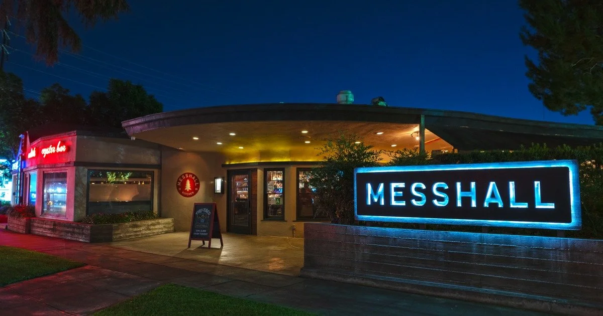 Nighttime exterior view of Messhall restaurant with illuminated sign, windows, and a small parking lot.