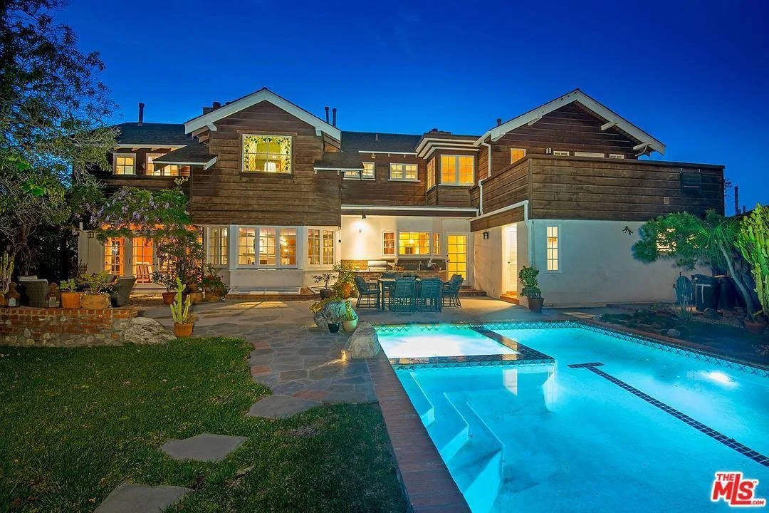 Backyard view of a two-story house with a swimming pool at dusk, outdoor seating area, potted plants, and a clear evening sky.