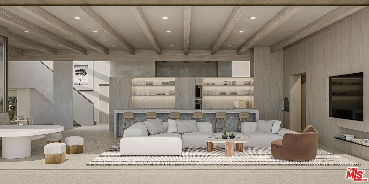 Modern, open-concept living room with a light color palette, white sofa, brown armchair, and a kitchen in the background with barstools, open shelving, and a gray countertop.