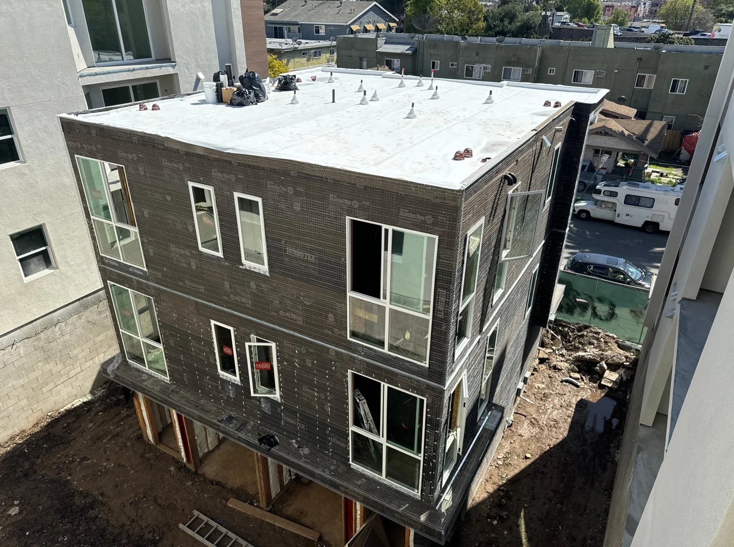 An aerial view of a three-story building under construction, with windows, a flat white roof, and exposed foundation and site work below.