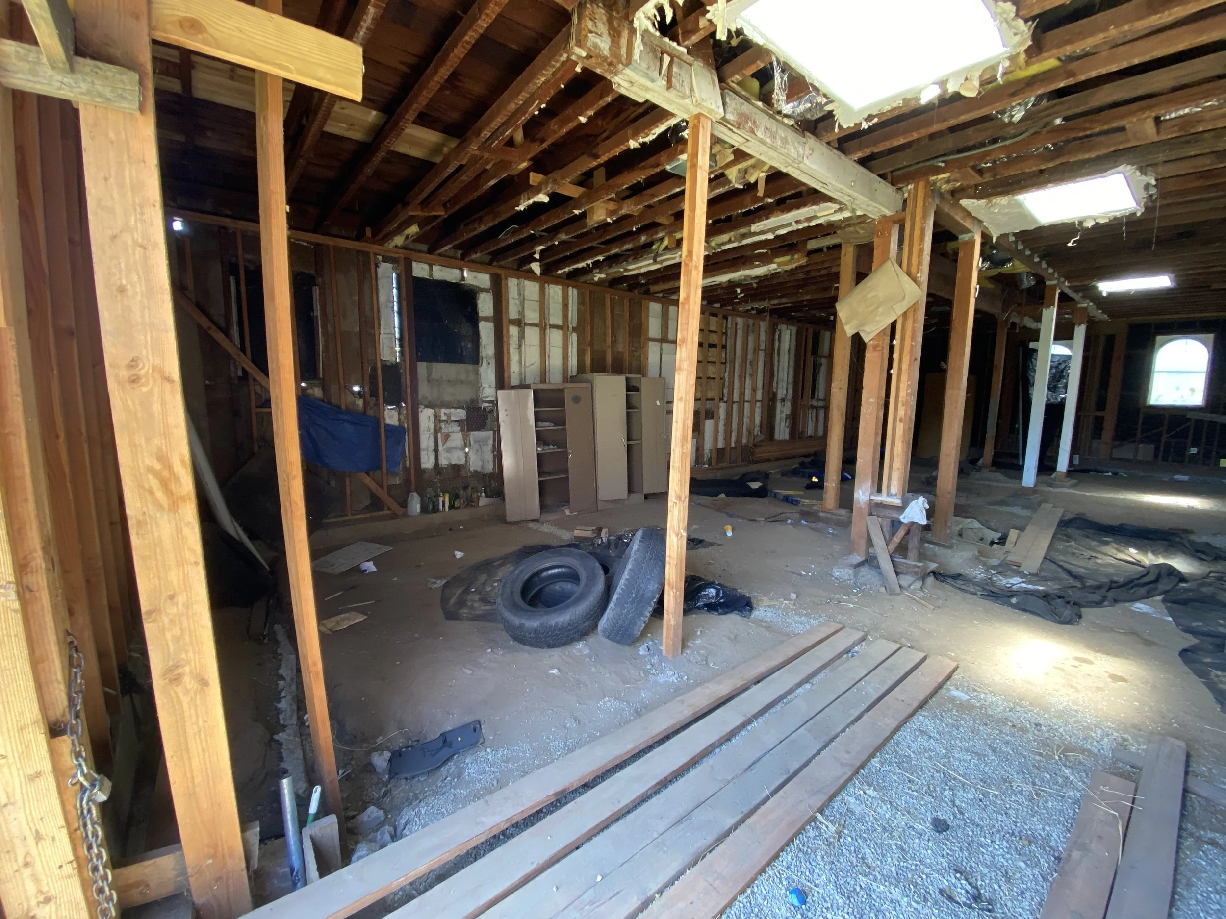 Interior of a building under construction with wooden framing, construction debris, tires, and a window showing sunlight outside.