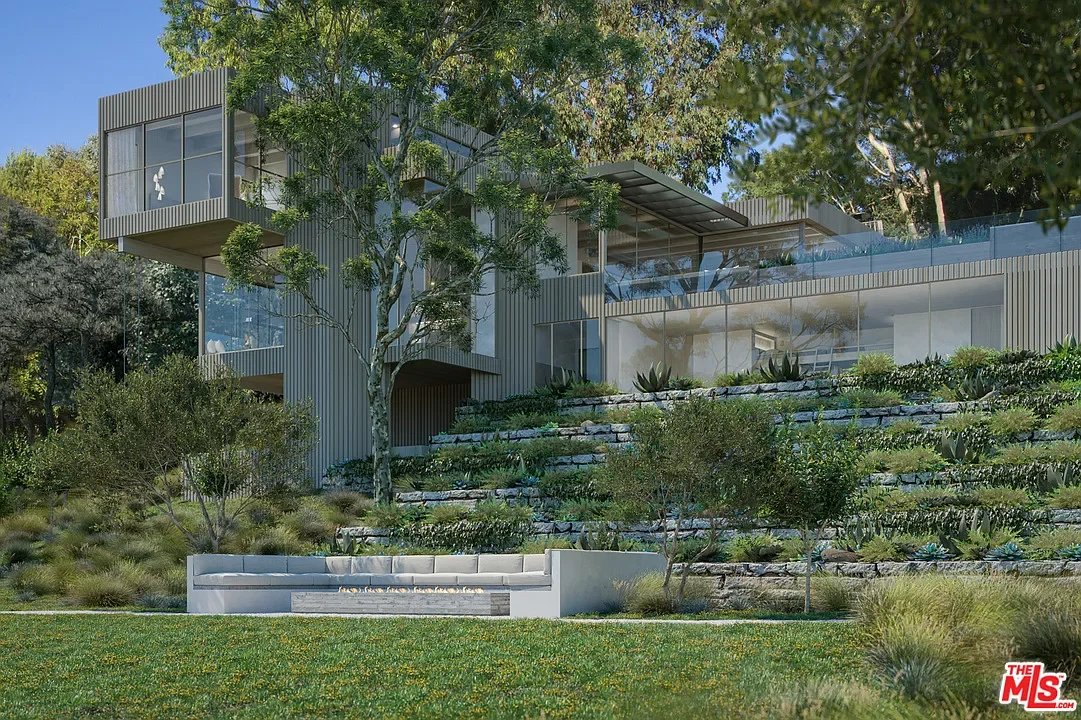 Modern multi-story house with large glass windows and a terrace, surrounded by trees and a landscaped yard with grassy areas and stone steps.