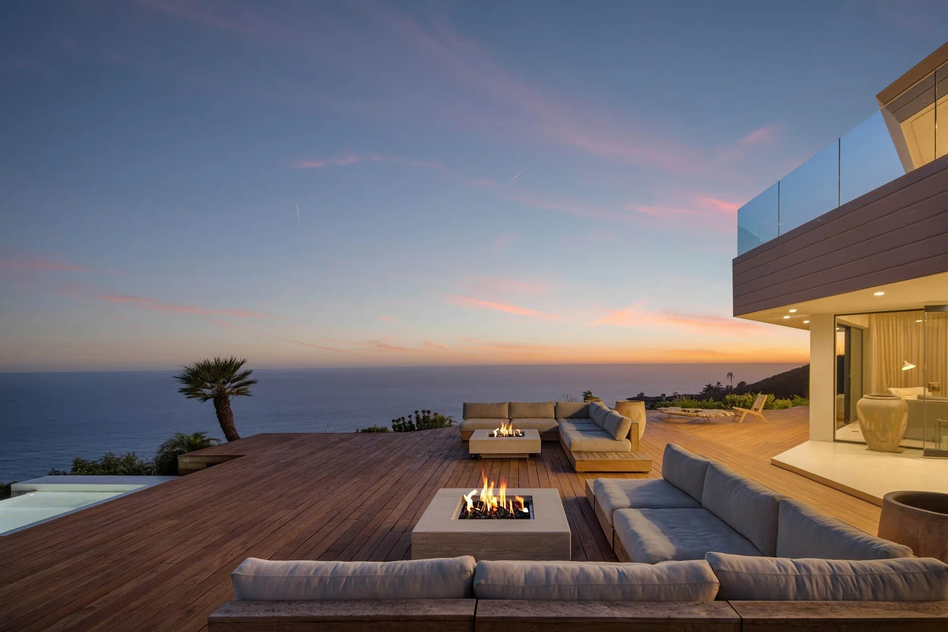 Luxury outdoor deck with seating area and two fire pits overlooking ocean at sunset