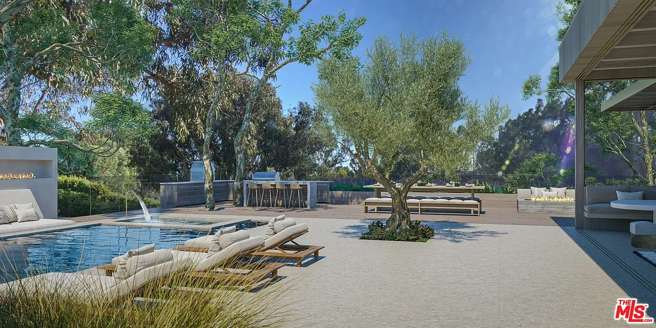 Luxury outdoor pool area with lounge chairs, a swimming pool with a waterfall feature, and surrounding trees and seating areas on a sunny day.