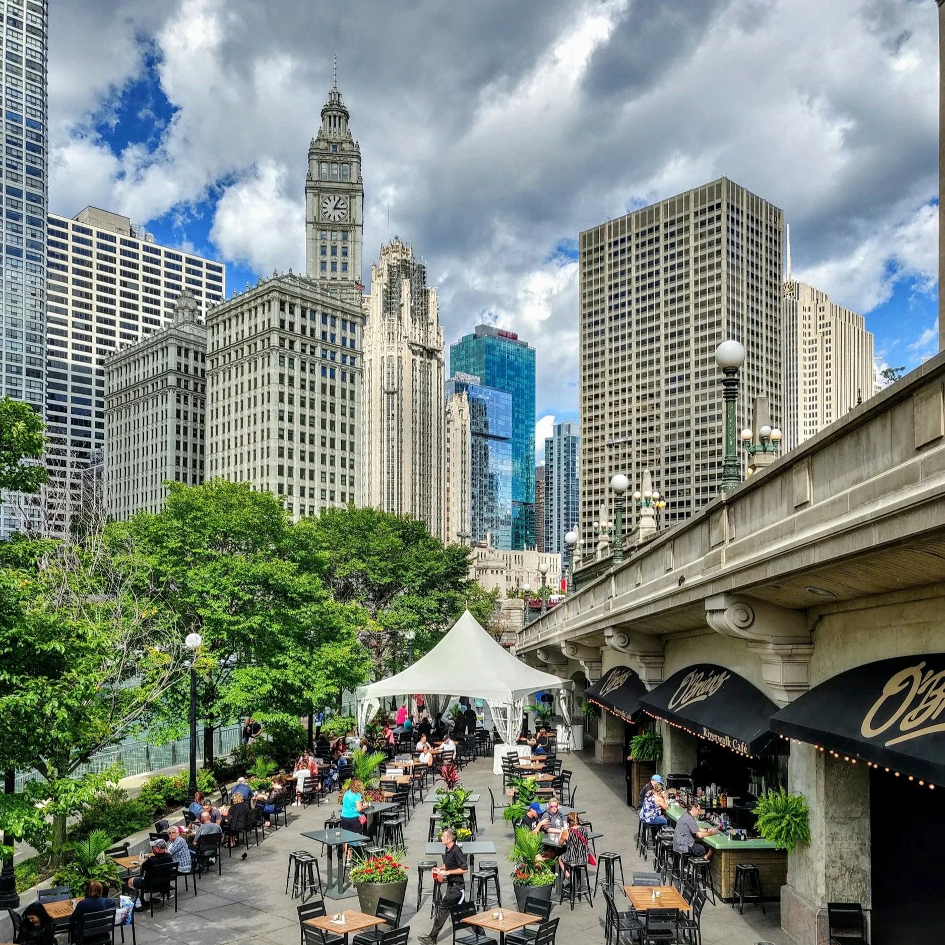 Outdoor patio scene along the Chicago River with city skyline and people dining, capturing the energy of springtime in downtown Chicago.