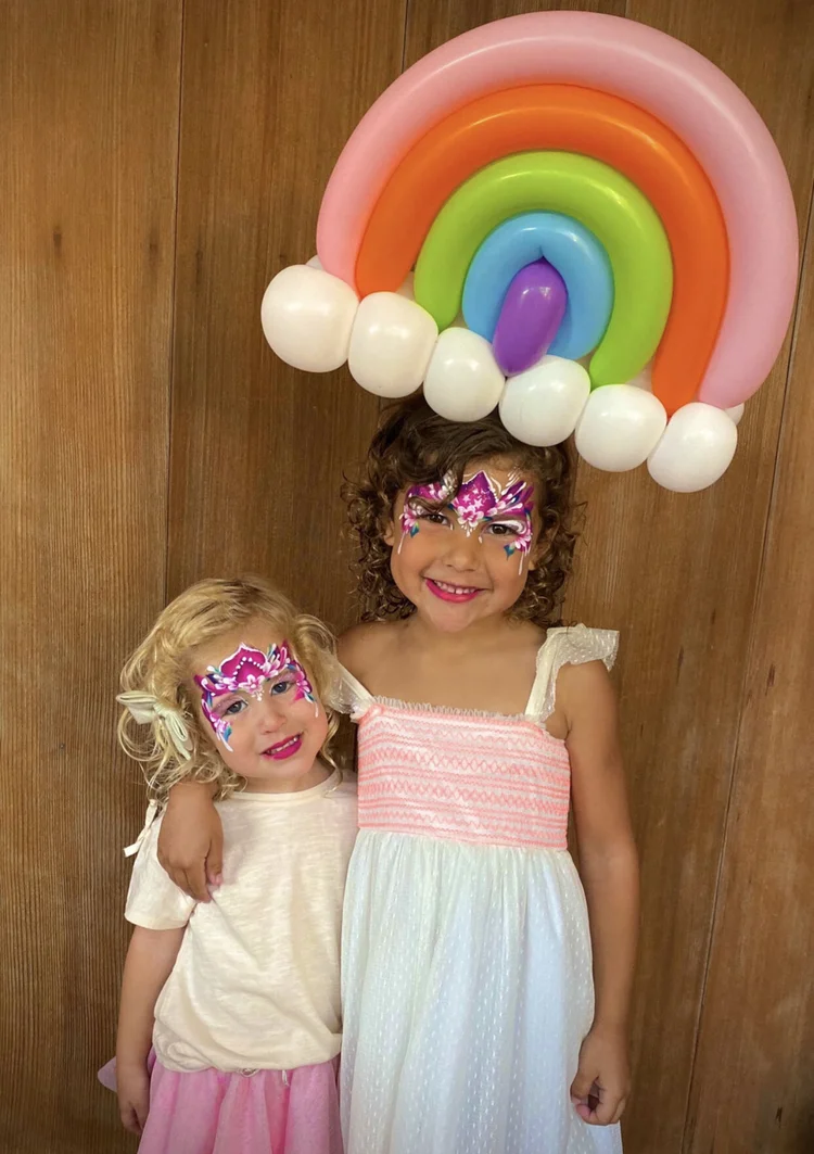 Two smiling girls holding a rainbow balloon creation at a DFW party