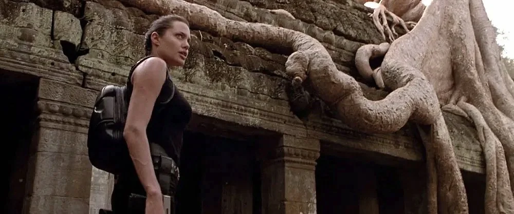 Lara Croft (Angelina Jolie) stands at Ta Prohm Temple at the Angkor Archaeological Park, image still from Lara Croft: Tomb Raider (2001). Via Paramount Pictures and Khreativa Cambodia (color-corrected).