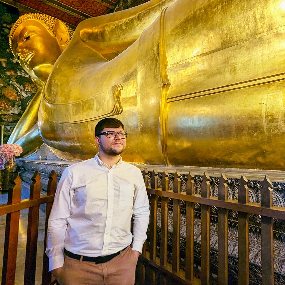  Posing with the 46-meter-long (151 feet) statue at Wat Pho (“Temple of the Reclining Buddha”), Bangkok, Thailand (2023). 