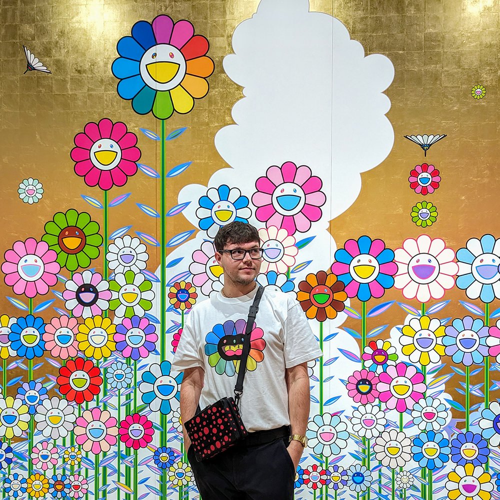  Posing with  Summer Flower Field under the Golden Sky,  acrylic and gold leaf on canvas mounted on wood panel, by Takashi Murakami (2023/24). 