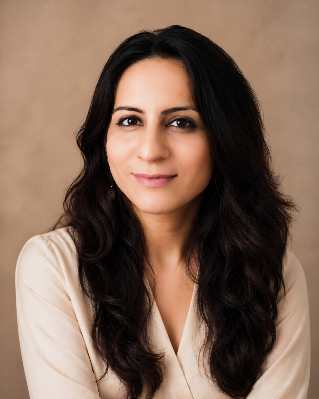 A woman with long dark hair and a slight smile, sitting beside stacked items in a cozy indoor setting.