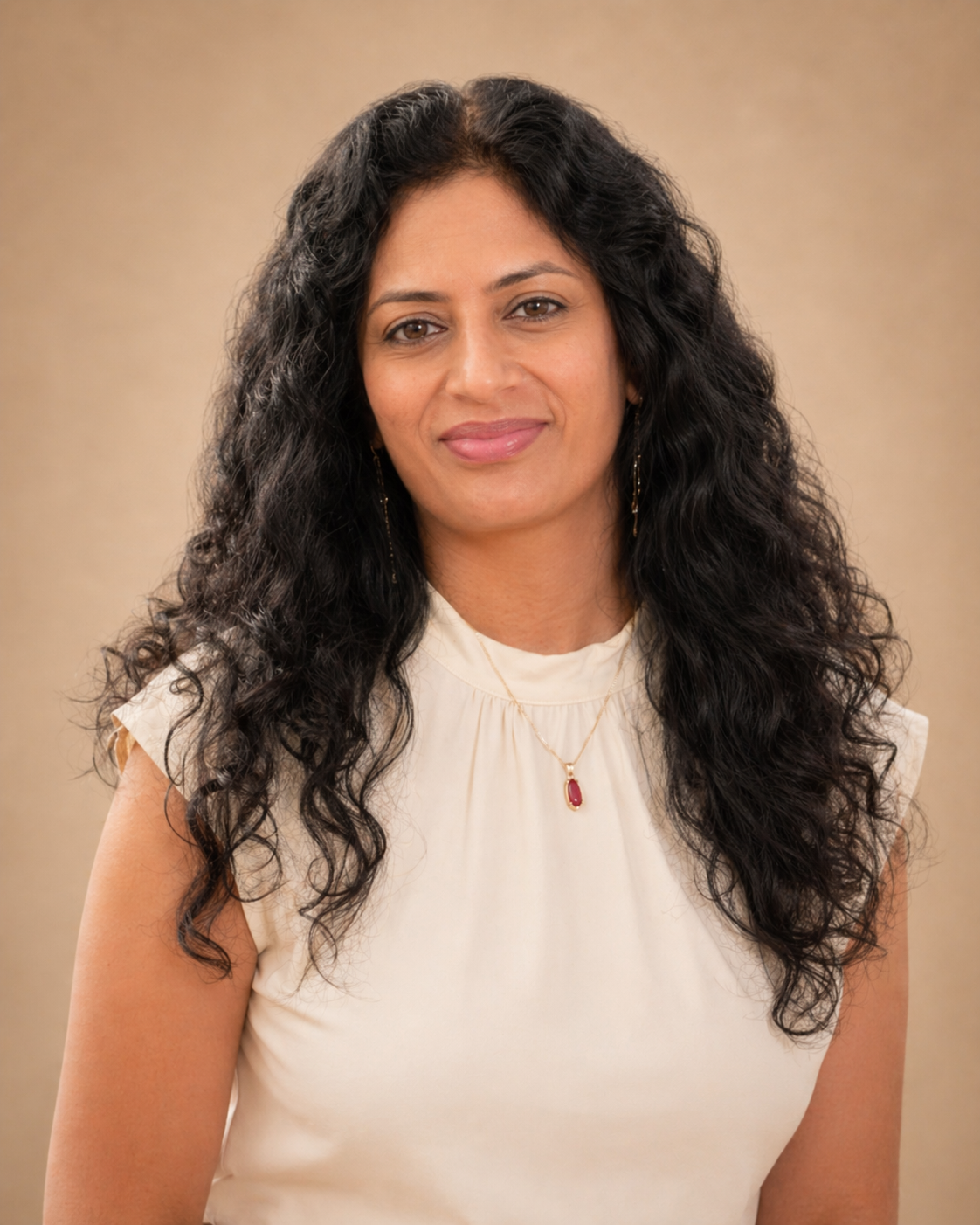 A woman with long dark curly hair wearing sunglasses, a white top with heart design, and light blue jeans standing in a sunflower field.