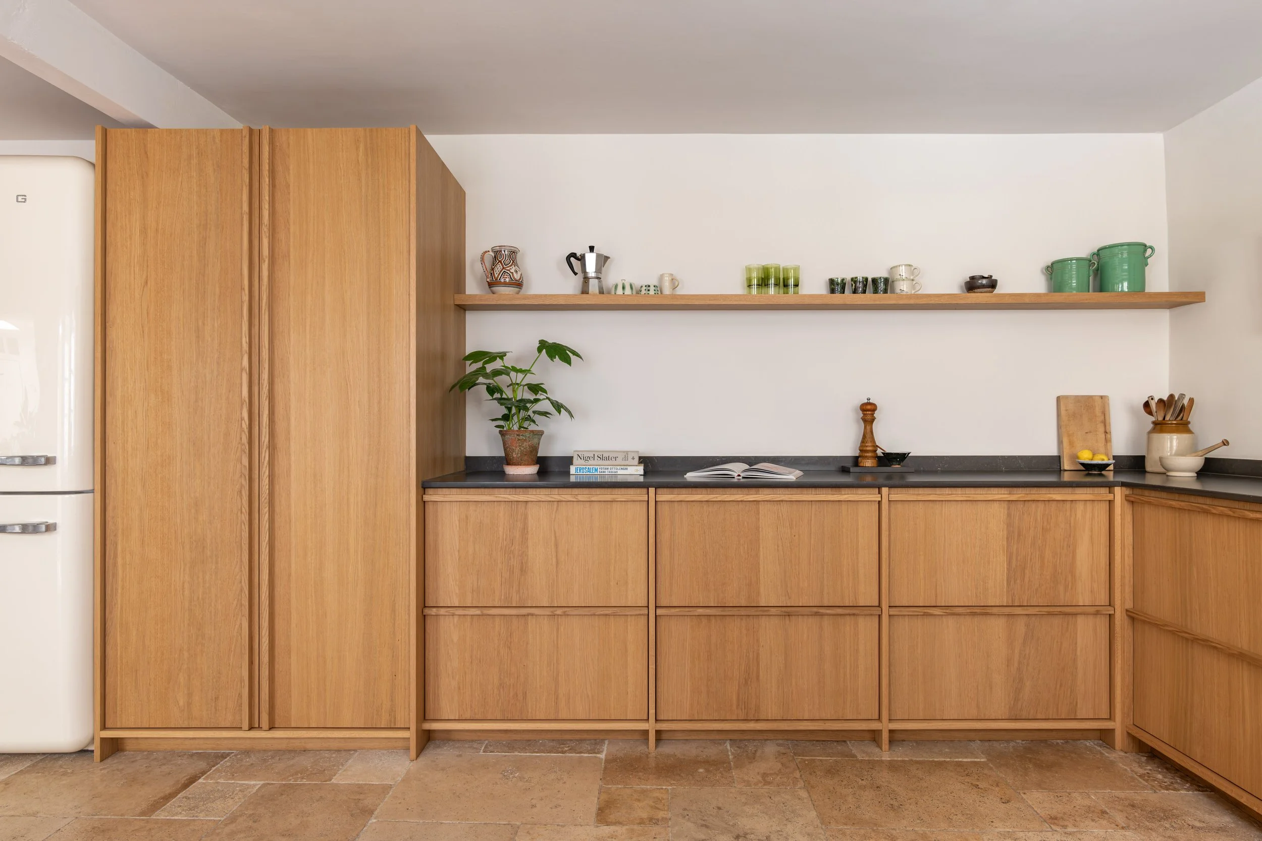 Bespoke oak kitchen cabinetry with integrated appliances, open shelving and dark stone worktops.
