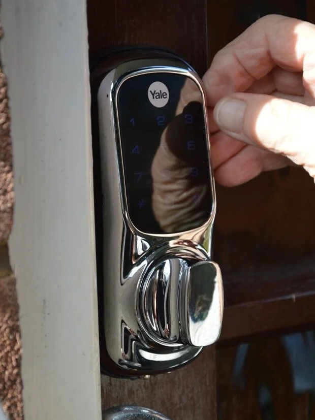 A Yale electronic keypad lock with a touchscreen, installed on a door, being operated by a person's hand.