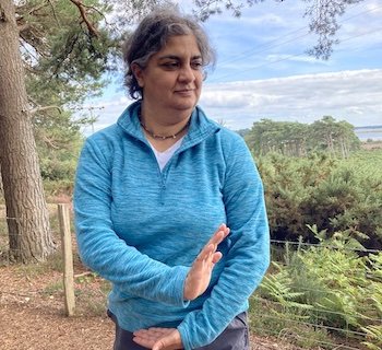 Rakhee practising a grounded Qigong movement outdoors among trees and greenery.