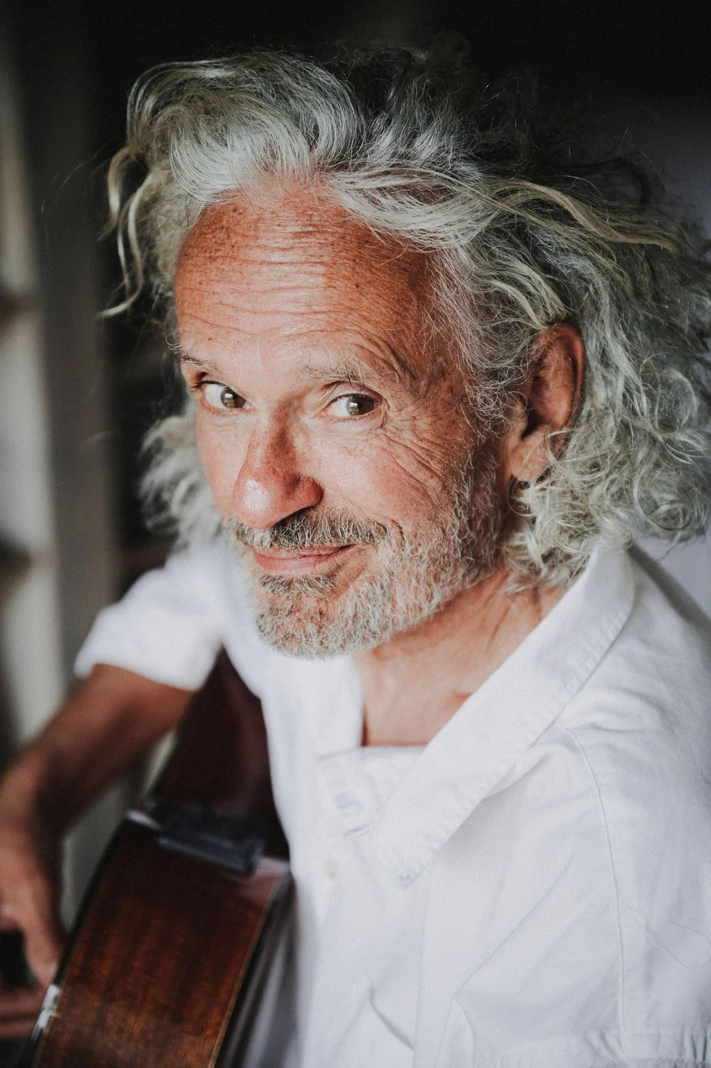 Mann mit grauem Haar spielt Gitarre und lächelt in die Kamera.