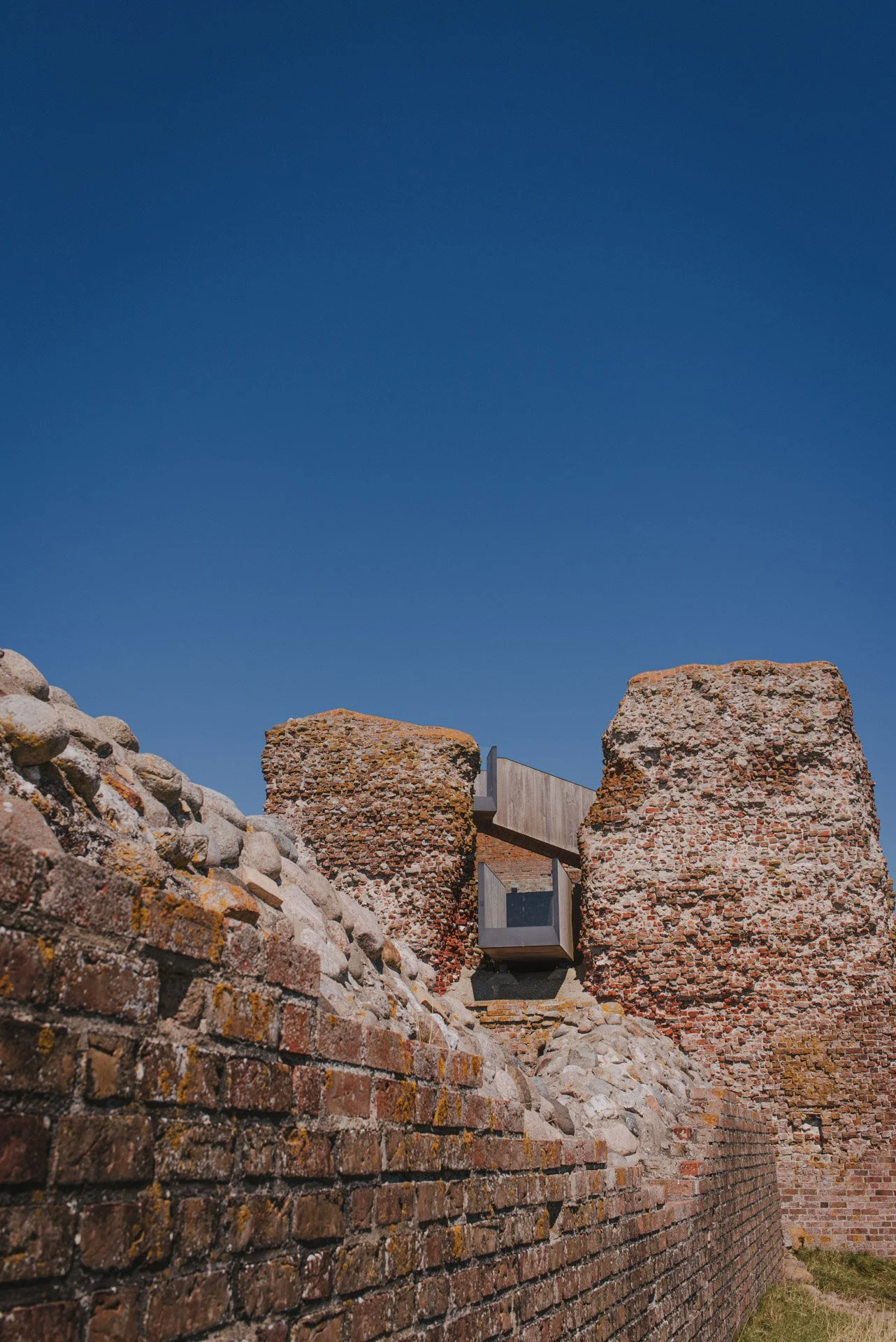 Alte Backsteinruinen mit modernem Glasdetail und blauem Himmel.