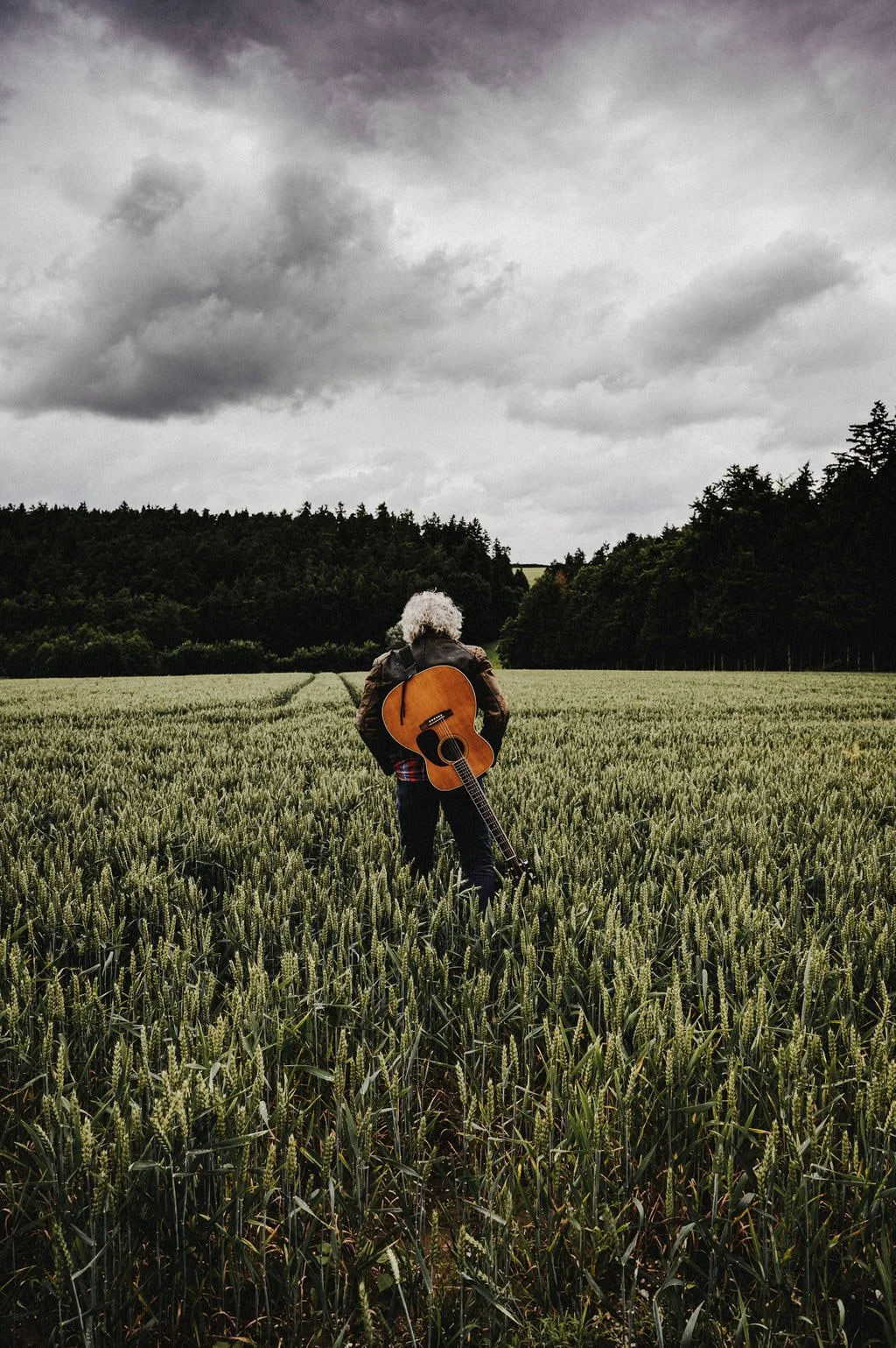 Mann mit Gitarre auf dem Rücken im Feld