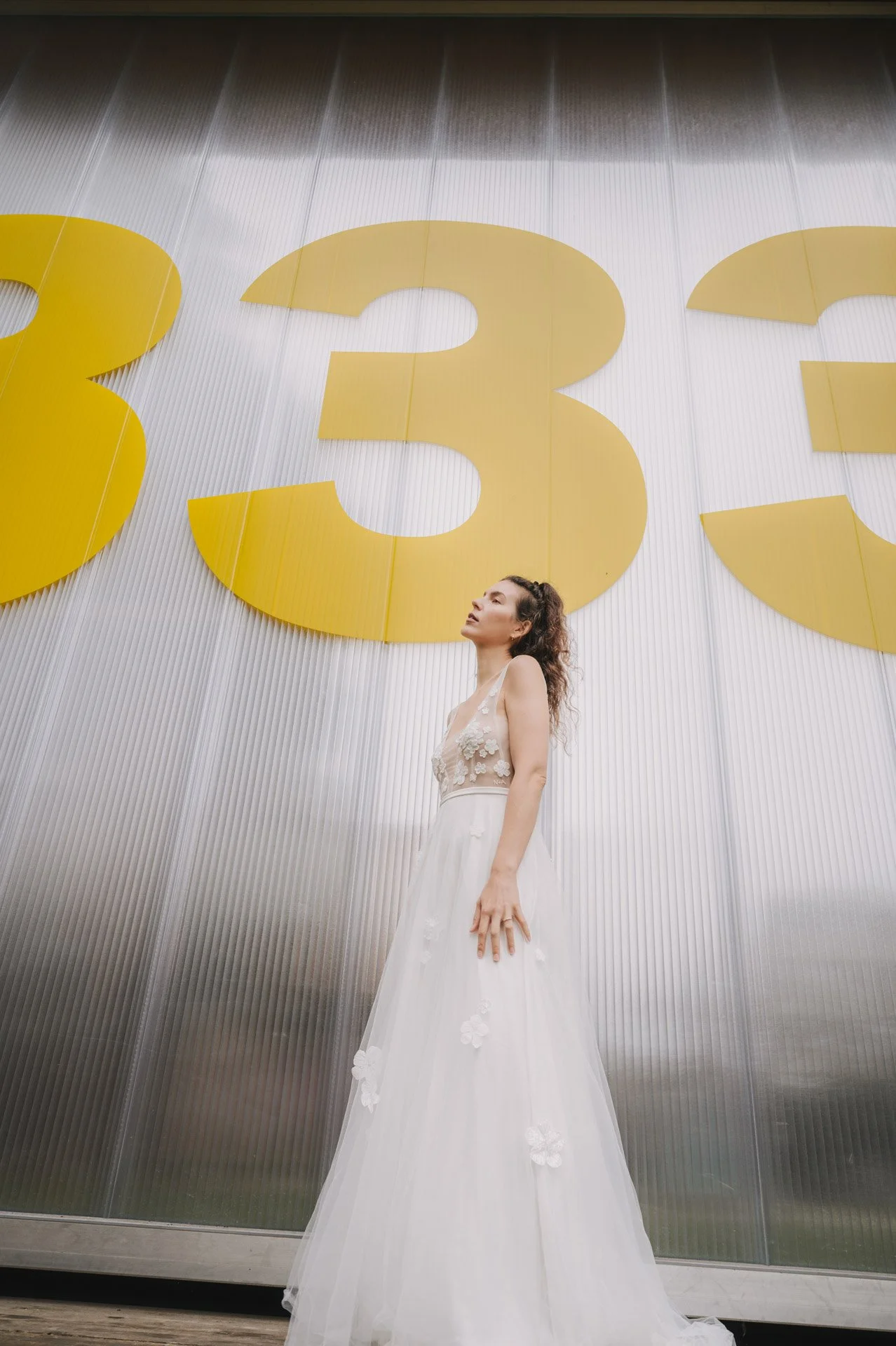 Frau in weißem Kleid steht vor großer gelber 33 auf silbernem Hintergrund.