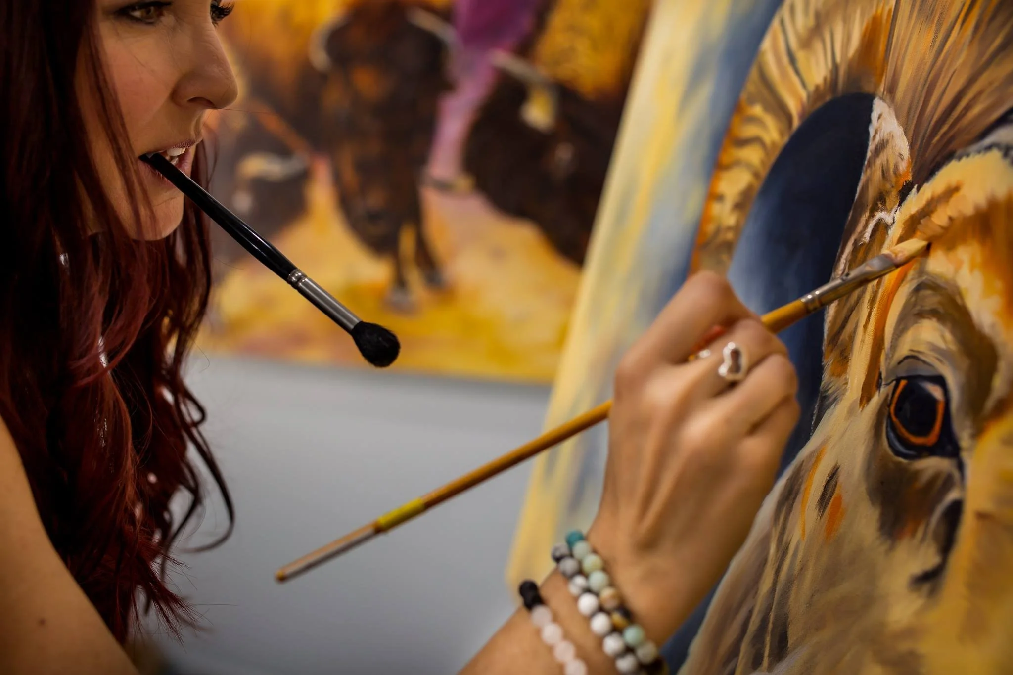 Woman with red hair painting a lion's face on a canvas in an art studio.