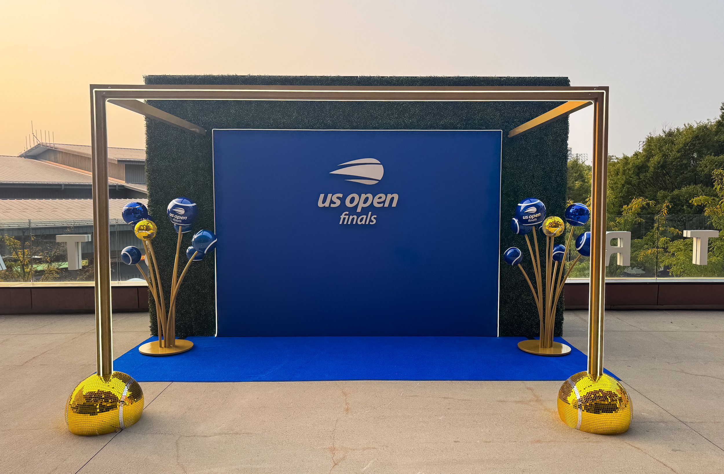 Stage setup for the US Open finals with blue backdrop, gold and blue balloons on both sides, and the US Open logo and text.