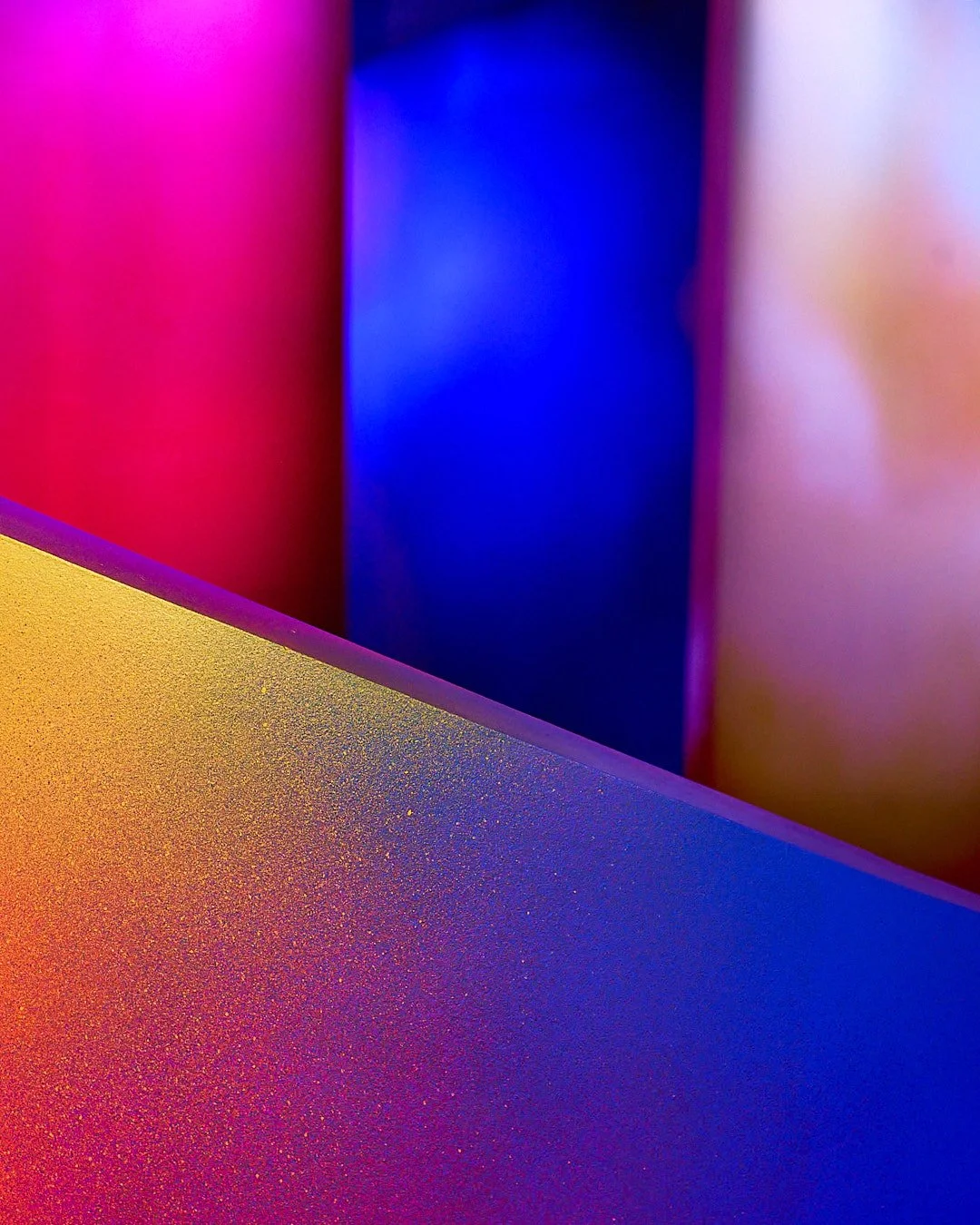 Close-up of colorful, textured, metallic surfaces with pink, purple, blue, and gold hues.