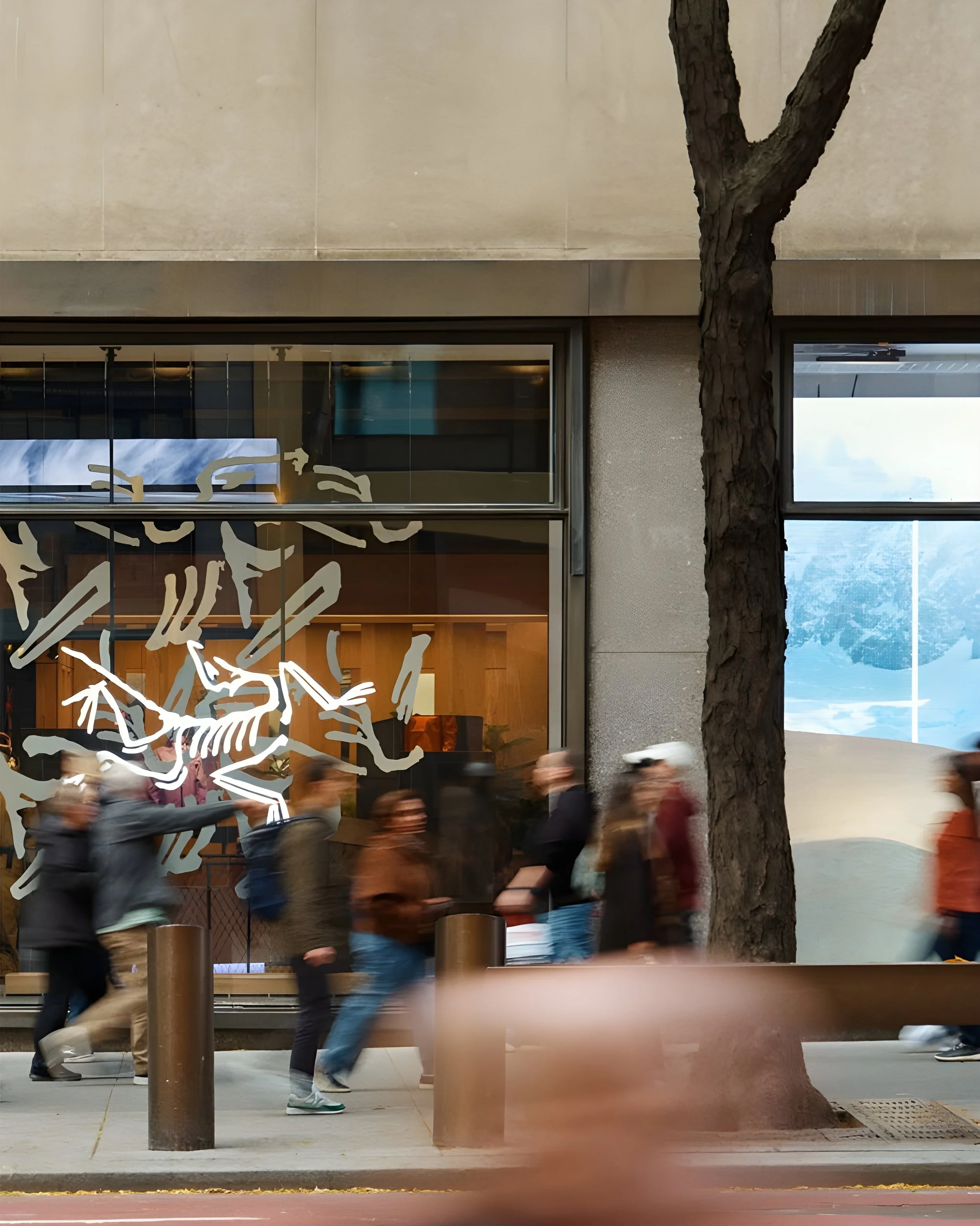 Pedestrians walking past a building with graffiti-covered glass window and a tree in front.
