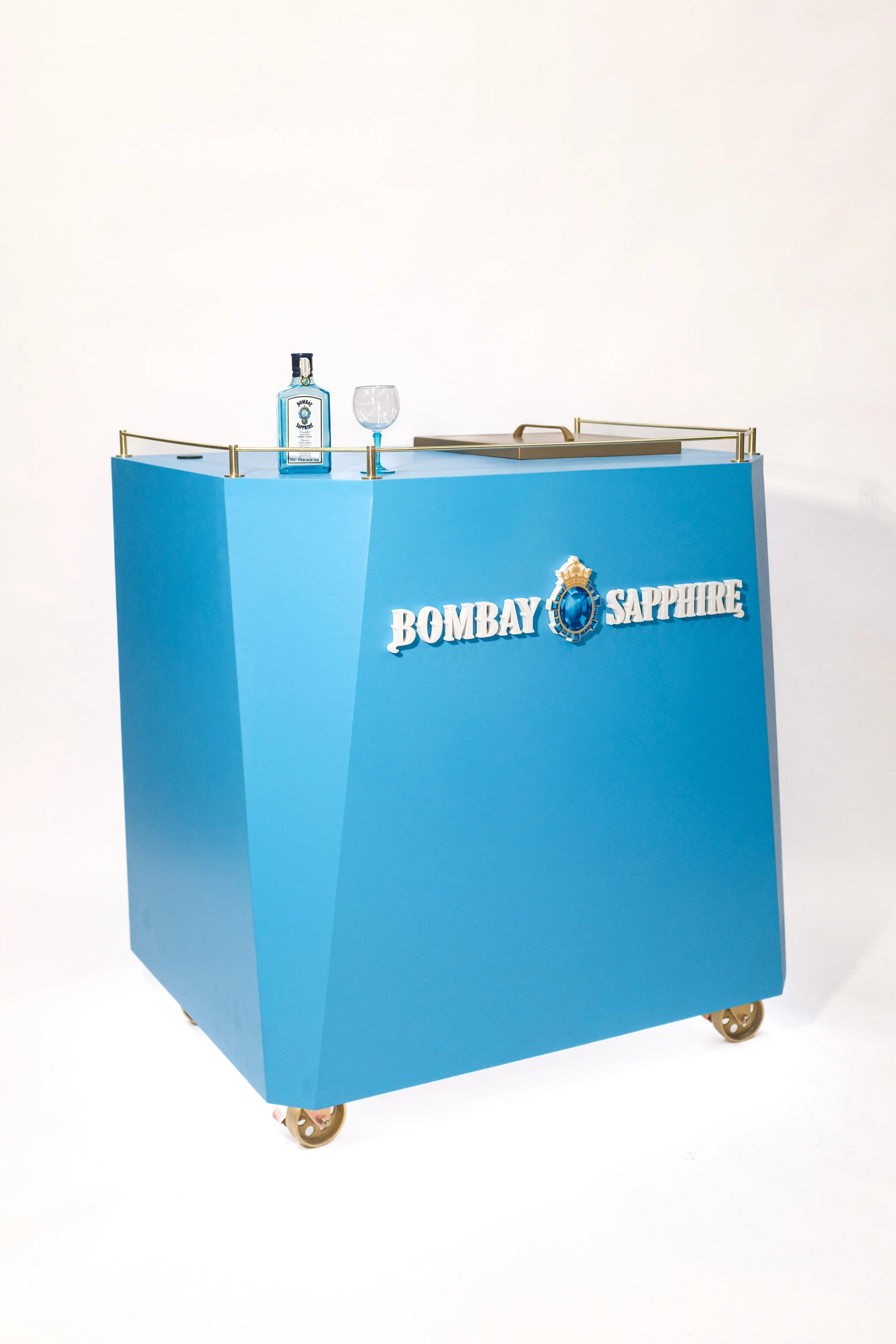 A blue Bombay Sapphire gin cart with a bottle and glass on top, and the brand logo in white on the front.