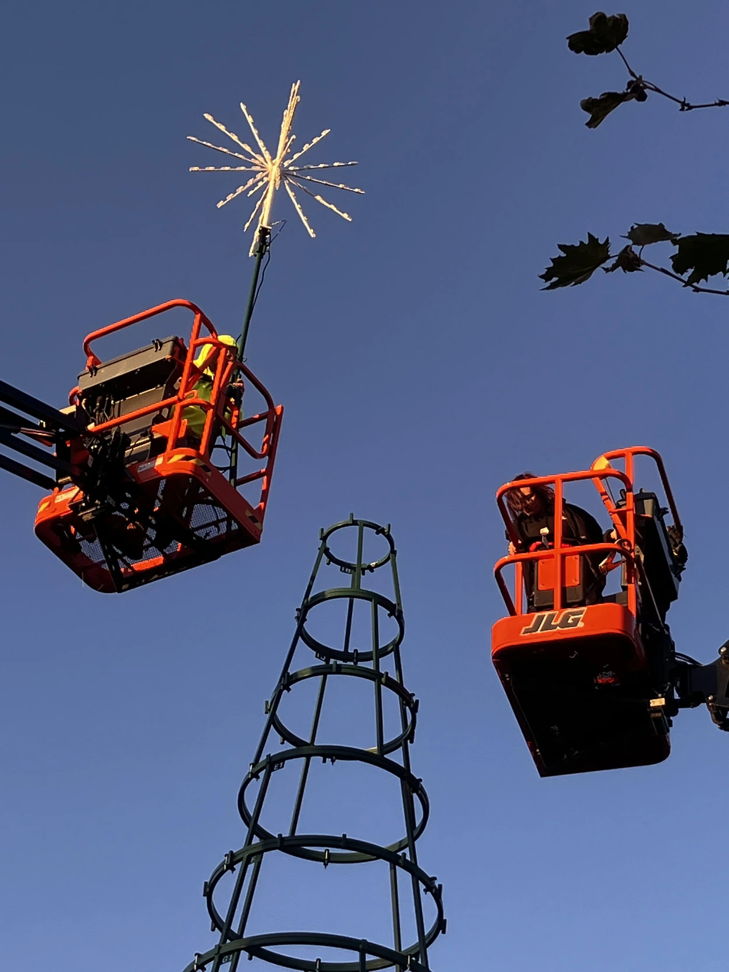 Two workers assemble a 42' Christmas Tree. Seen here topping off the tree with a star.