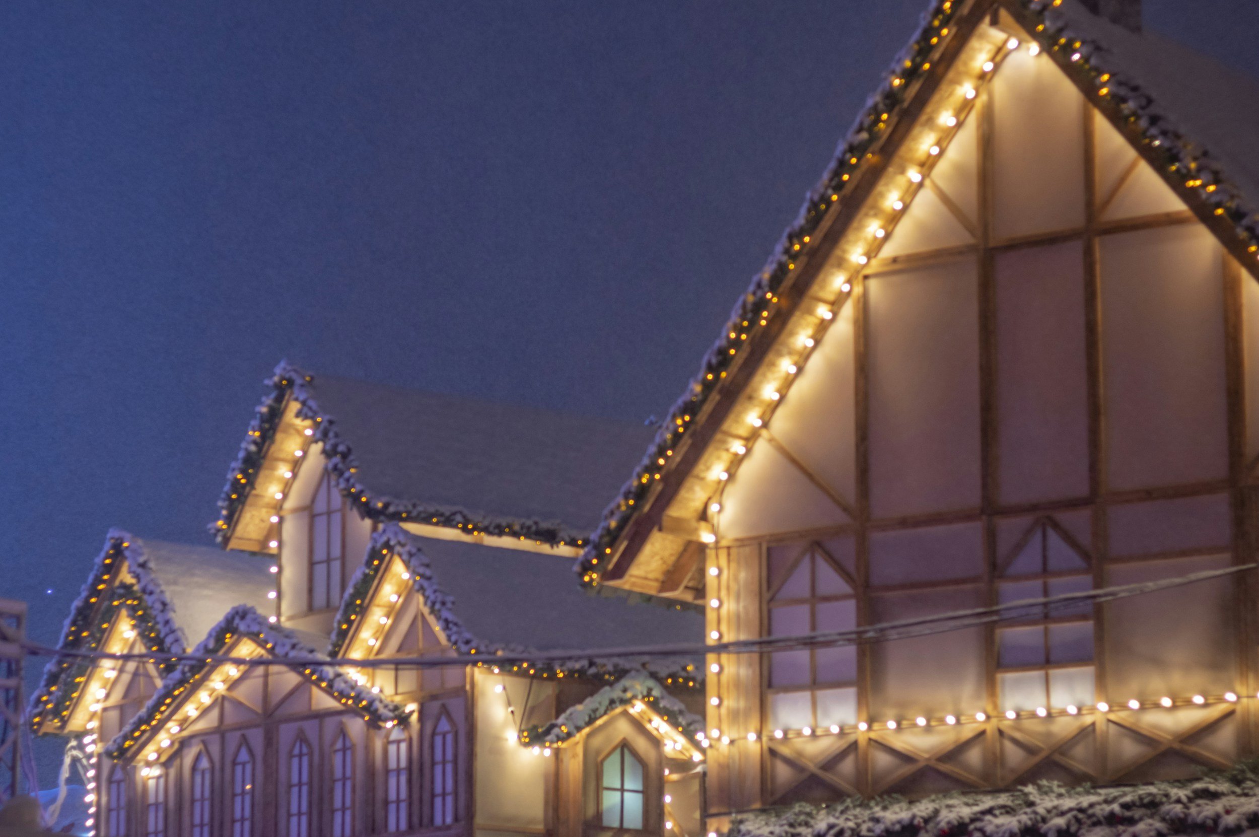 A wooden chalet-style house decorated with Christmas lights and snow, at night.