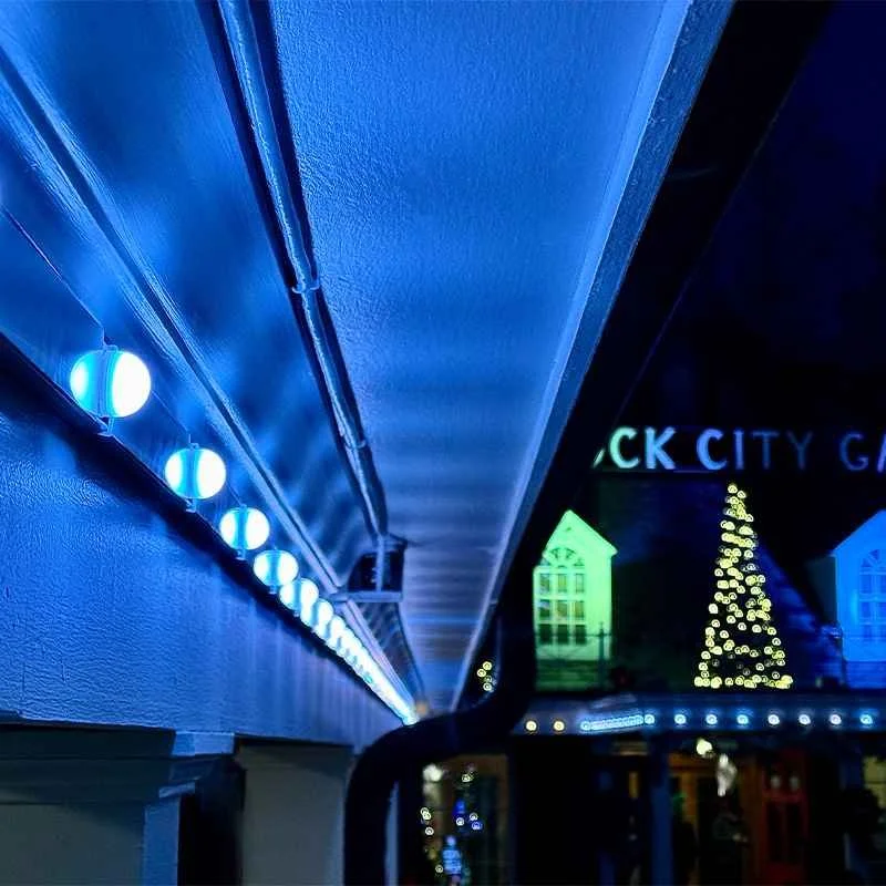 Night scene of a building with blue lights and Christmas decorations, including a Christmas tree and lit-up house shapes, with partially visible sign reading 'CK CITY.'