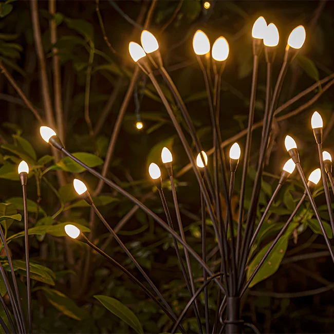 A cluster of outdoor string lights with small glowing bulbs hanging among green leaves at night.