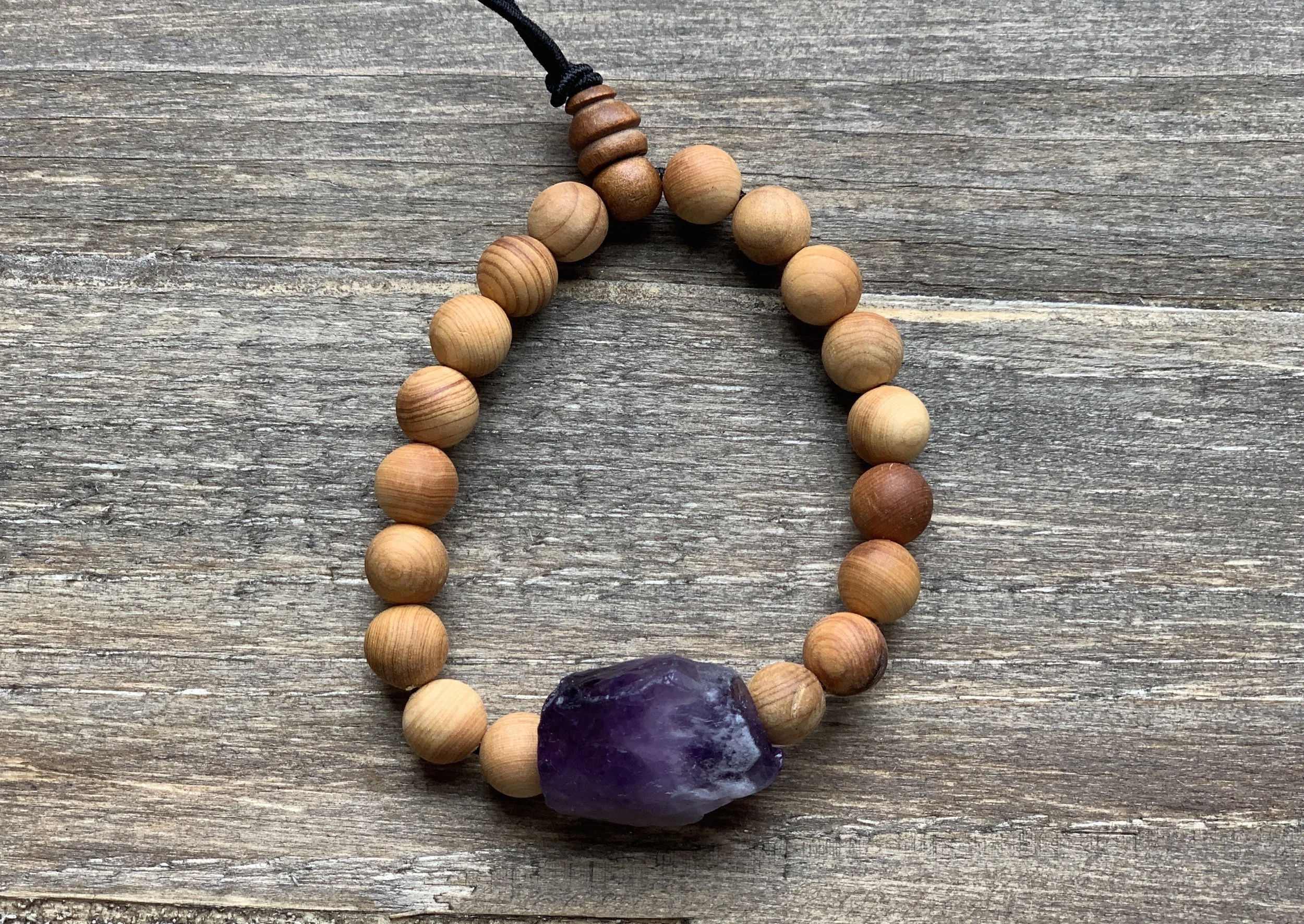 Wooden beaded bracelet with a large purple gemstone on a wooden surface.