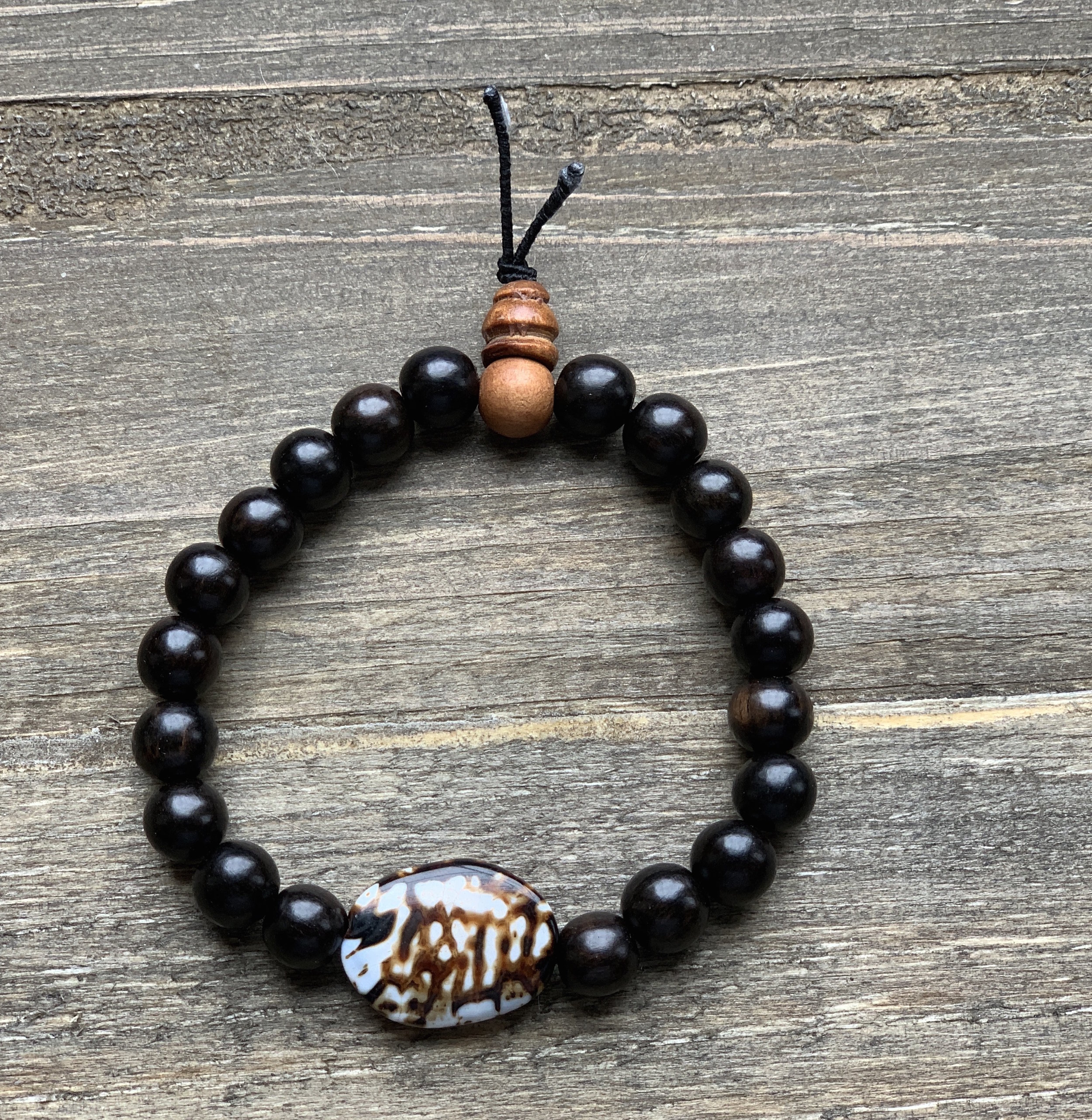Beaded necklace with dark brown beads, a carved stone pendant with white and brown pattern, and wooden bead accent, on a wooden surface.