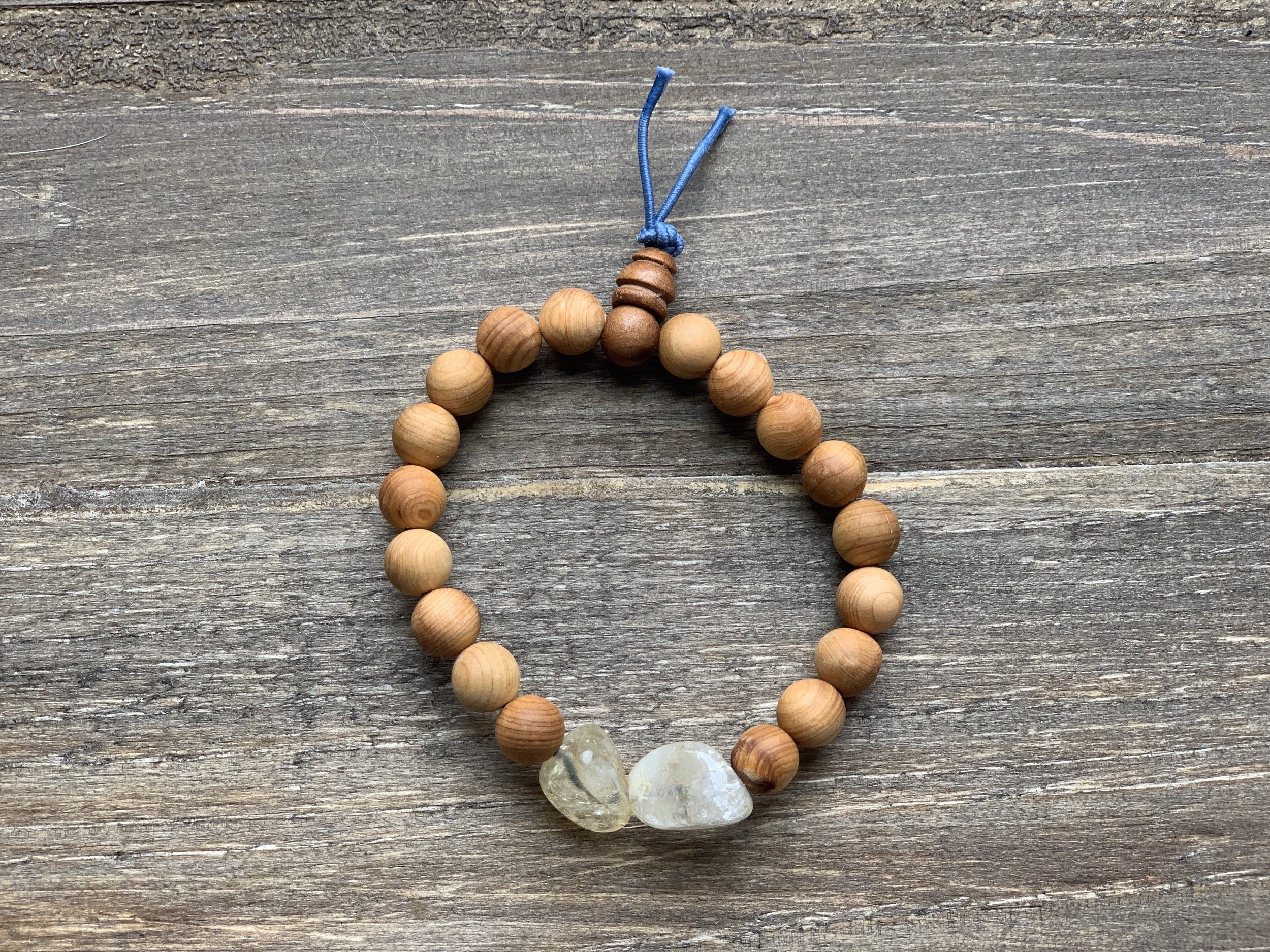 Beaded bracelet with small wooden beads and two larger clear stones, tied with a blue string on a wooden surface.