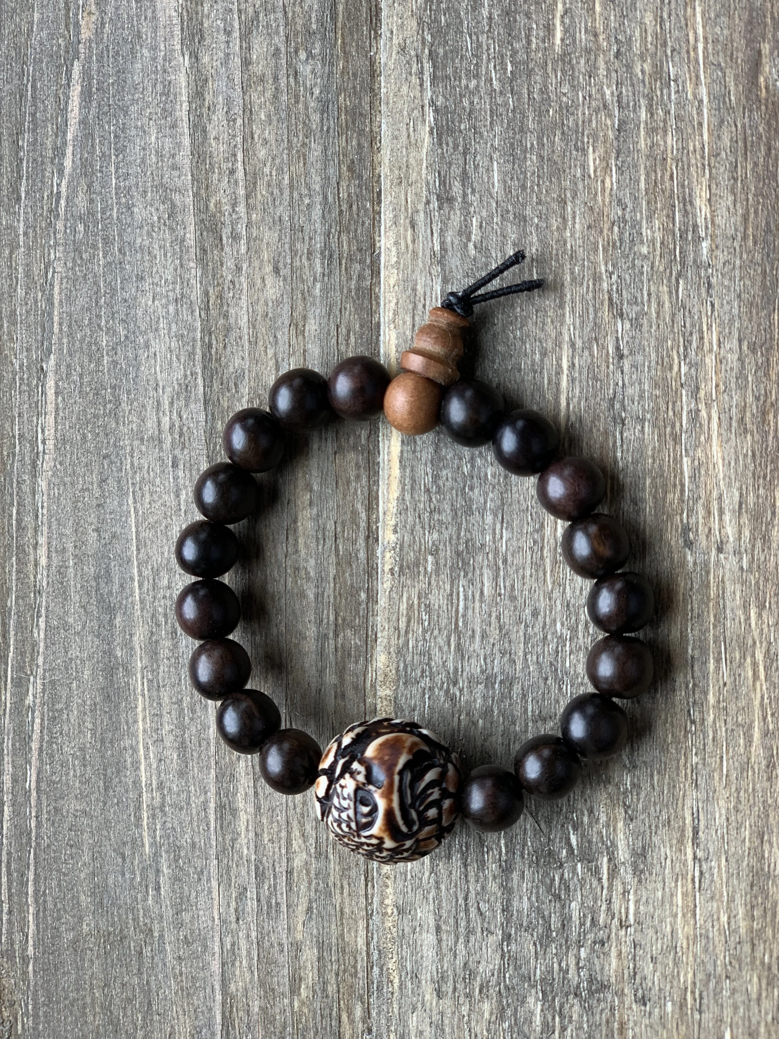 A beaded bracelet with dark brown beads, a carved bead with swirls, and a small wooden piece with a string.