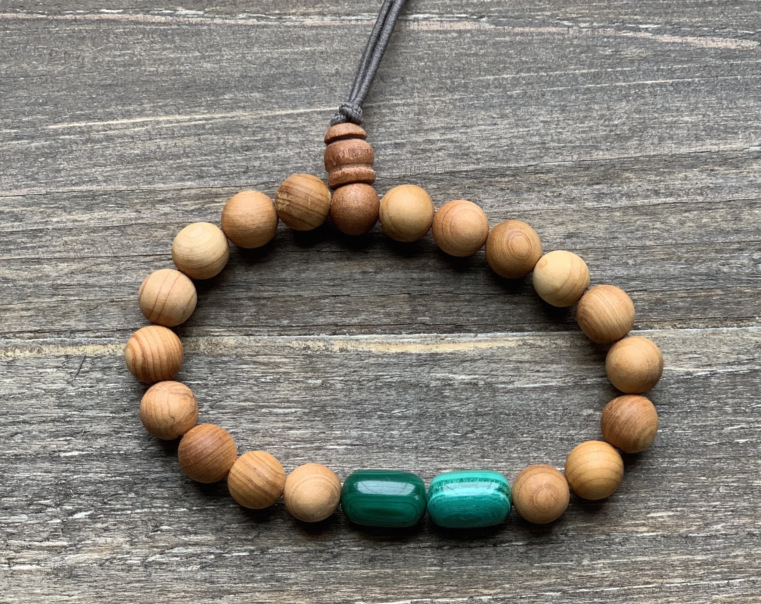 A beaded necklace made of light brown wooden beads with two larger turquoise beads, displayed on a weathered wooden surface.