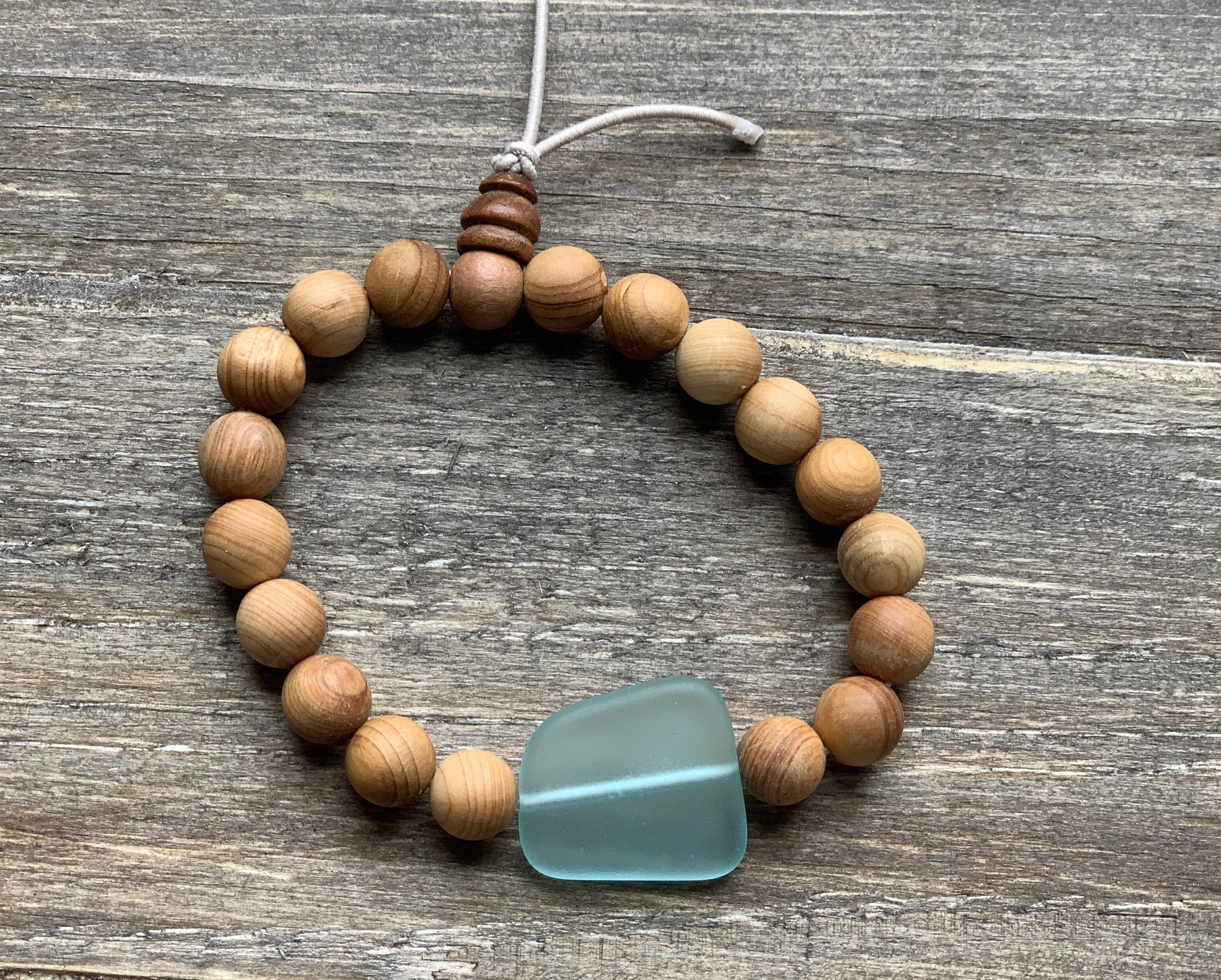 Beaded bracelet made of round wooden beads with a large light blue gemstone or glass piece, connected by a white cord, resting on a wooden surface.