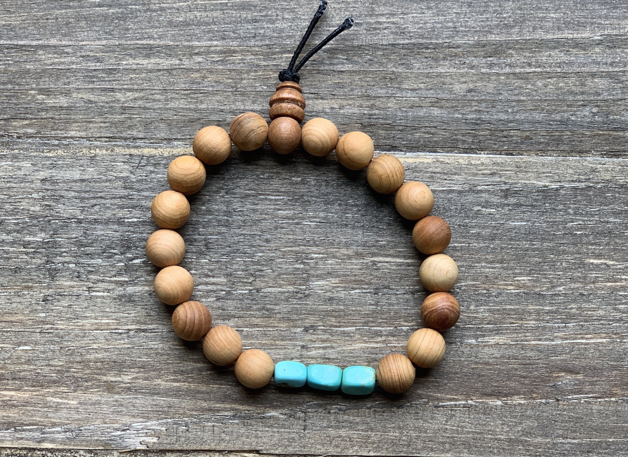 Beaded bracelet made of round wooden beads and three turquoise beads on a wooden surface.